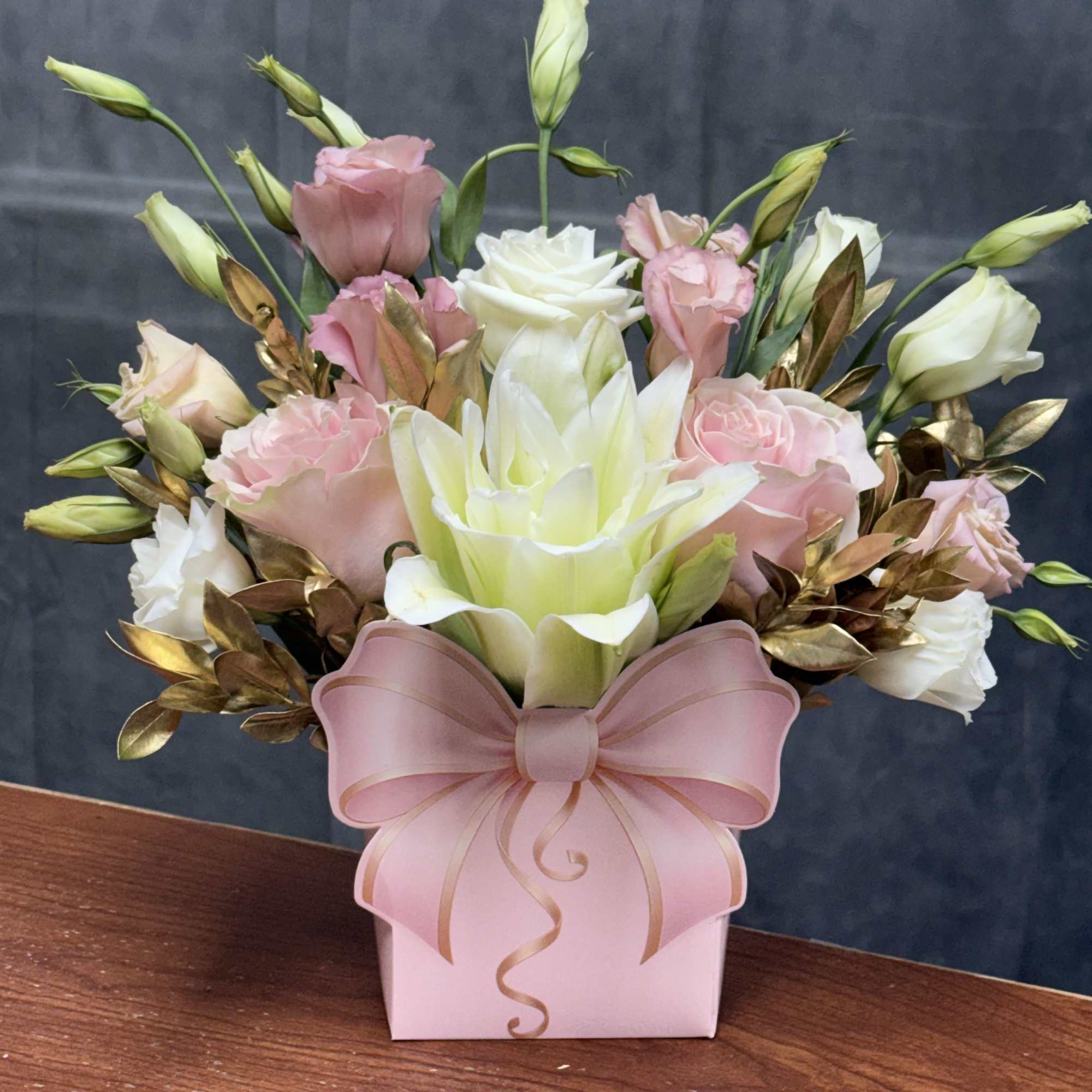 A luxurious arrangement featuring blush roses, white lilies, and golden foliage for