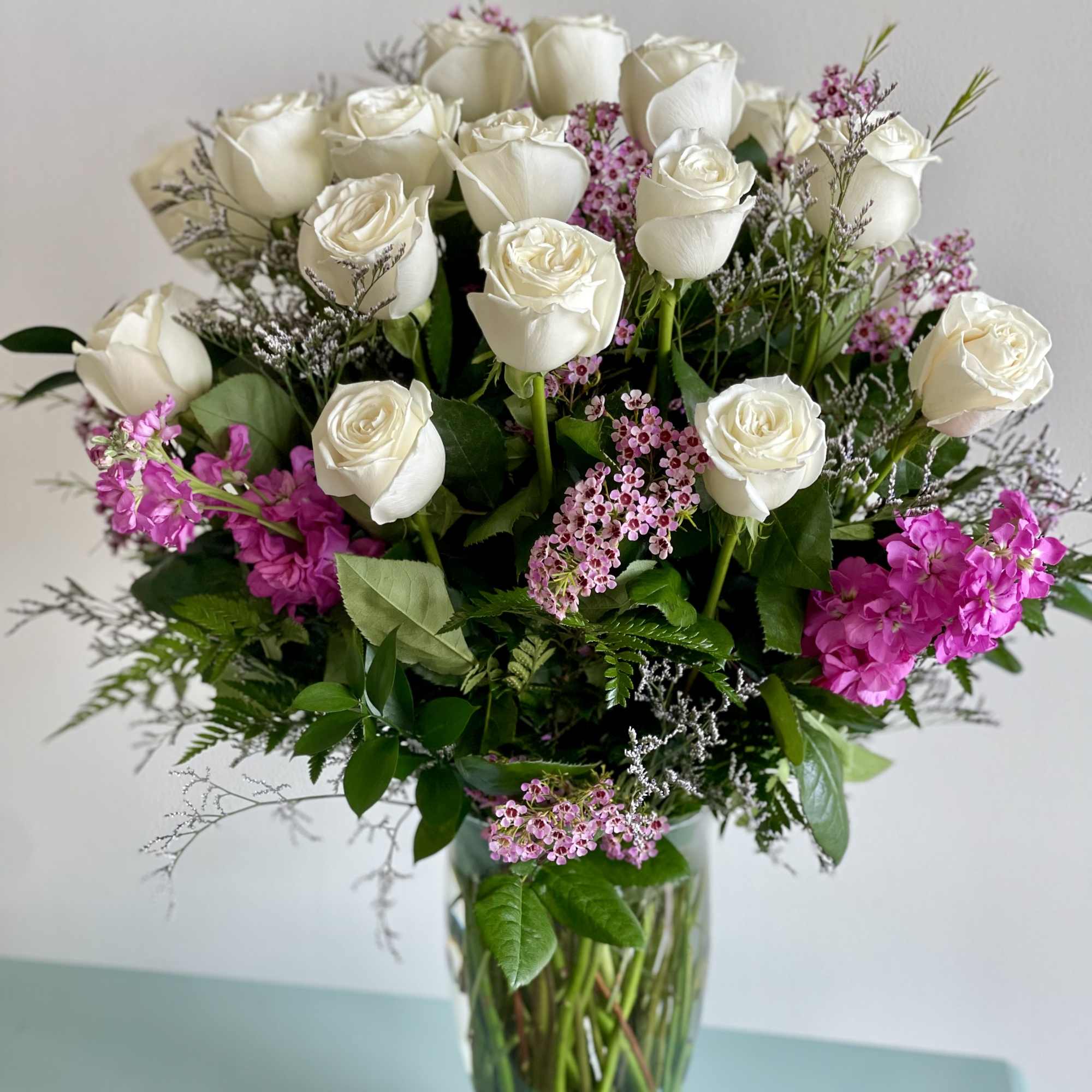 White roses and pink filler flowers arranged in a clear glass vase