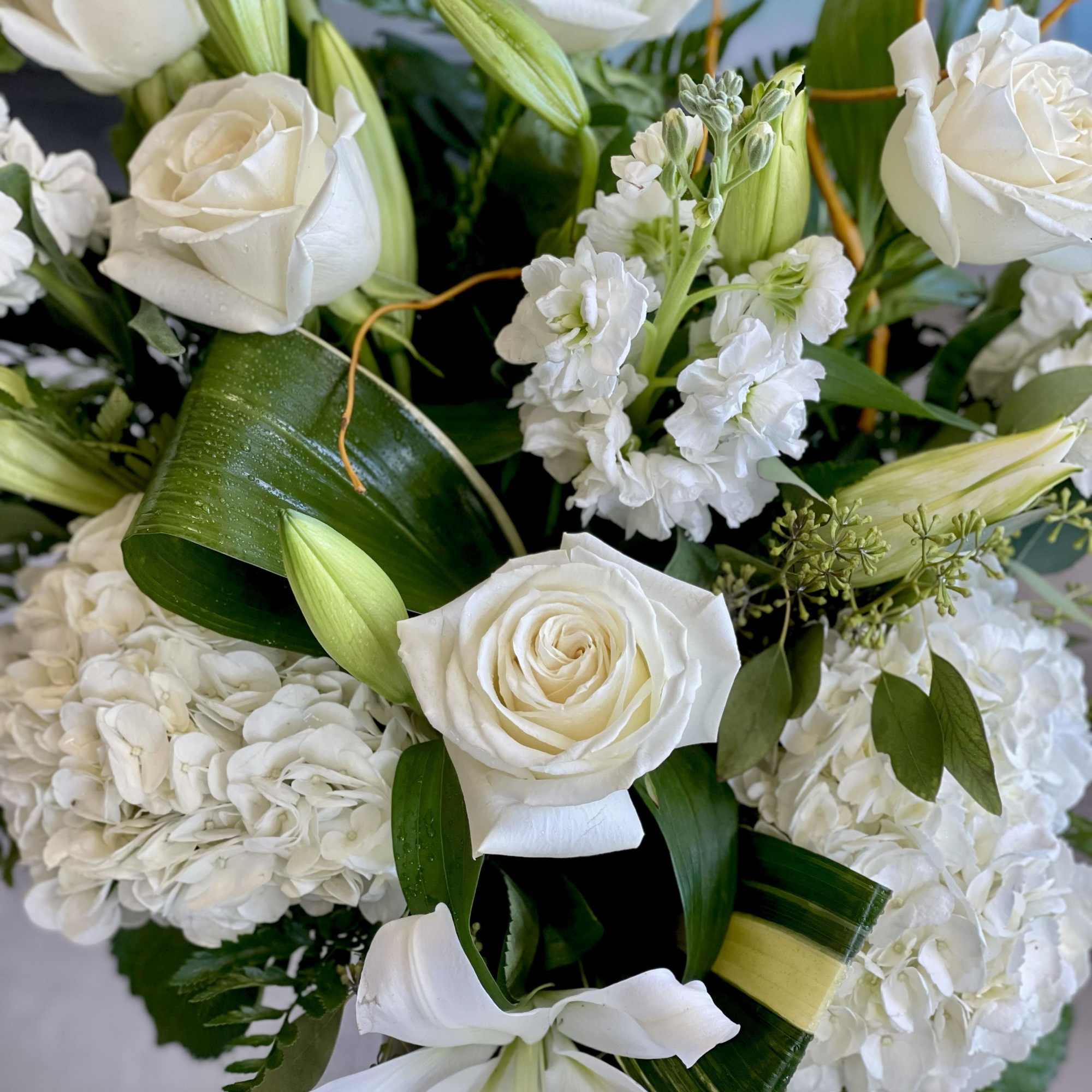 White roses and lilies arranged with hydrangeas and greenery