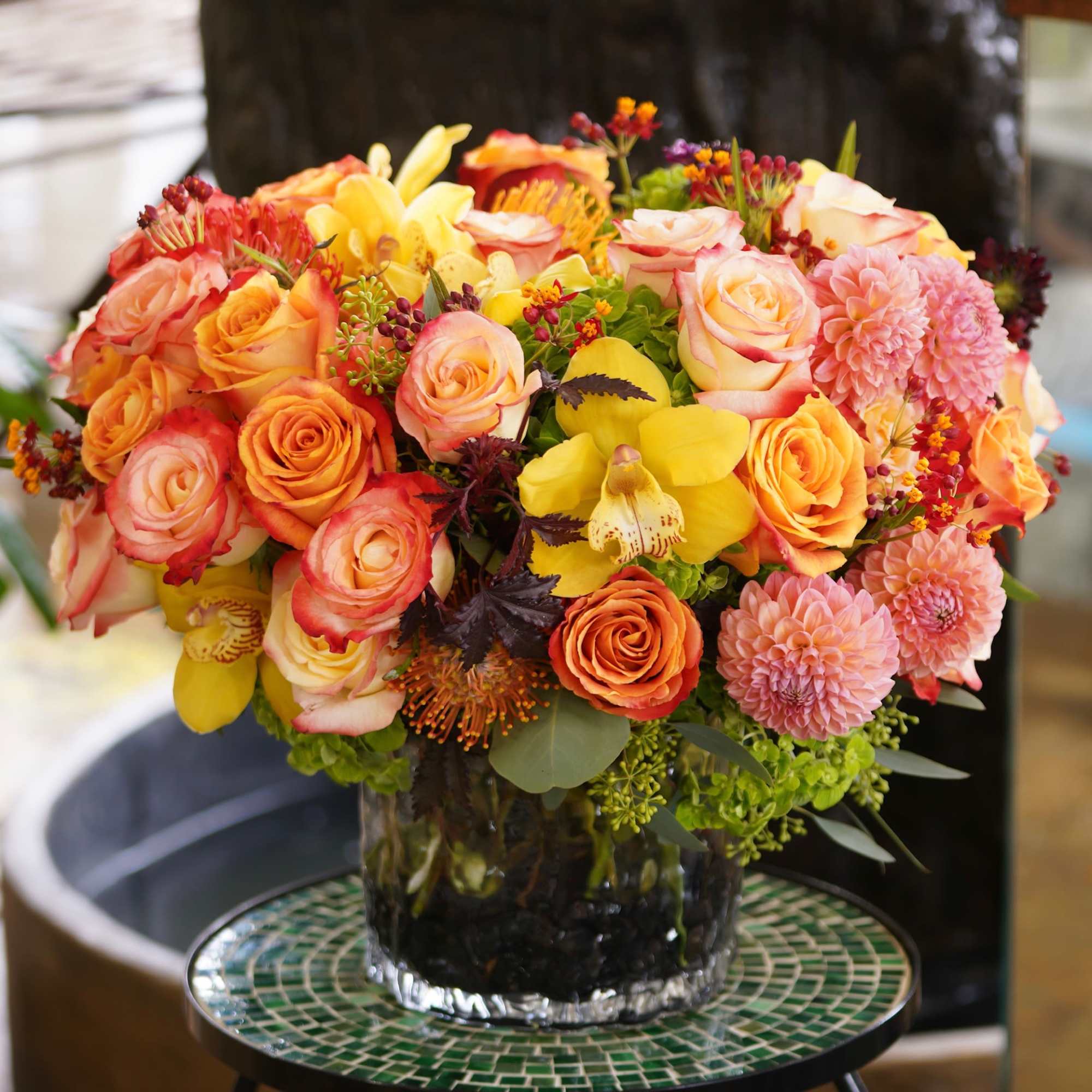 Mixed bouquet of roses, orchids, and pink dahlias in a glass vase