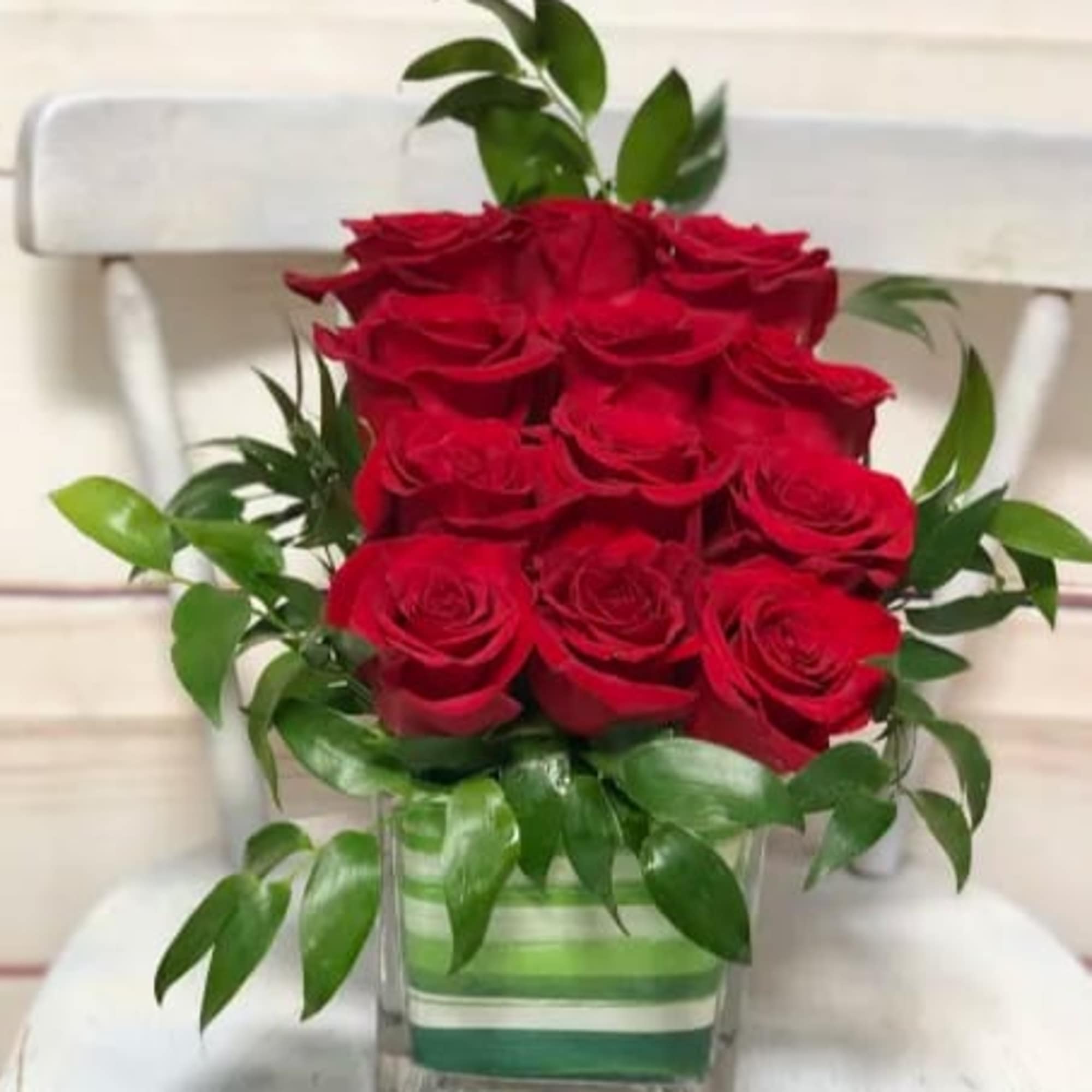Red roses arranged in a clear square vase with green foliage
