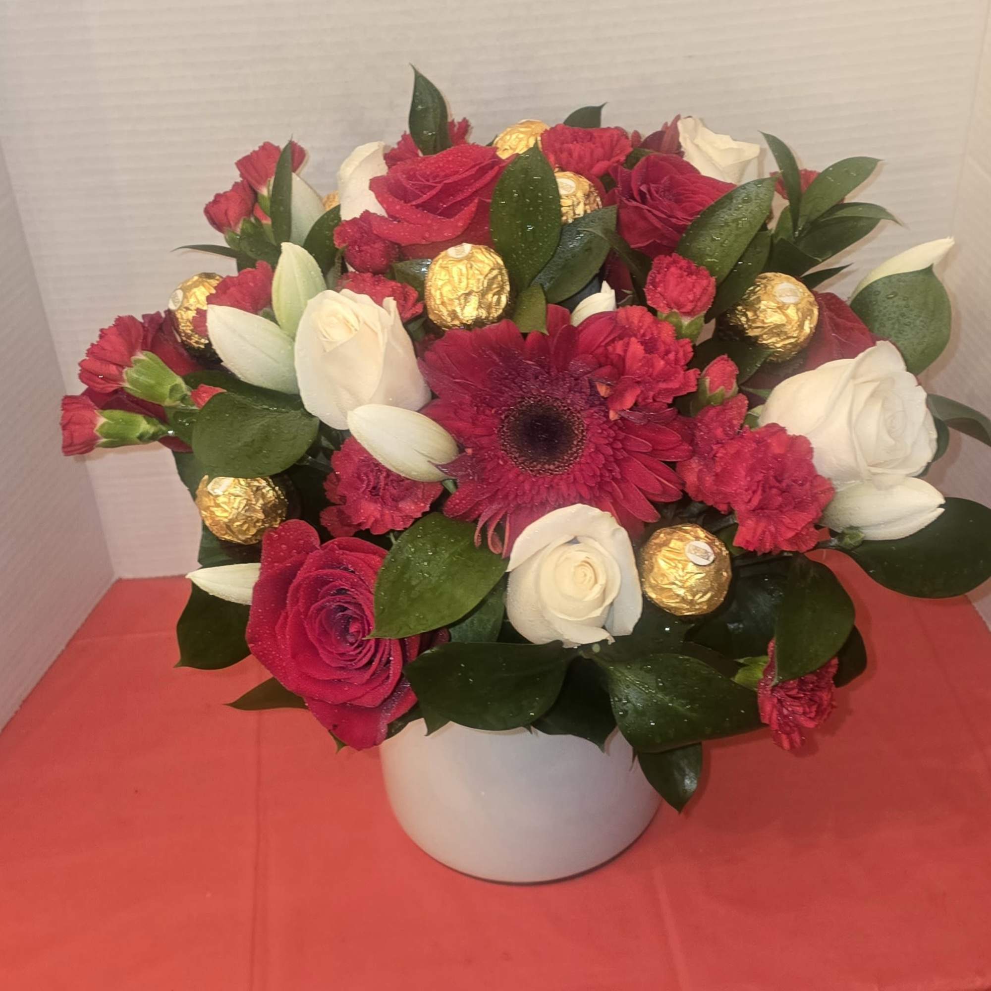 Bouquet of red and white flowers in a white vase with gold chocolates