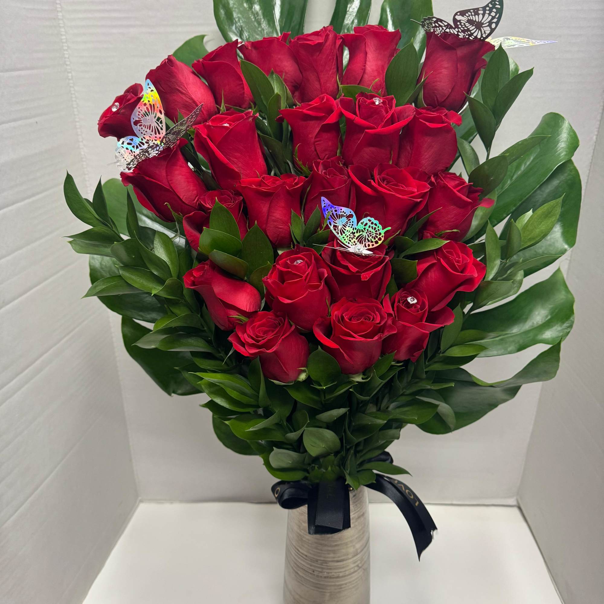 Bouquet of red roses in a tall vase with green foliage and butterfly picks