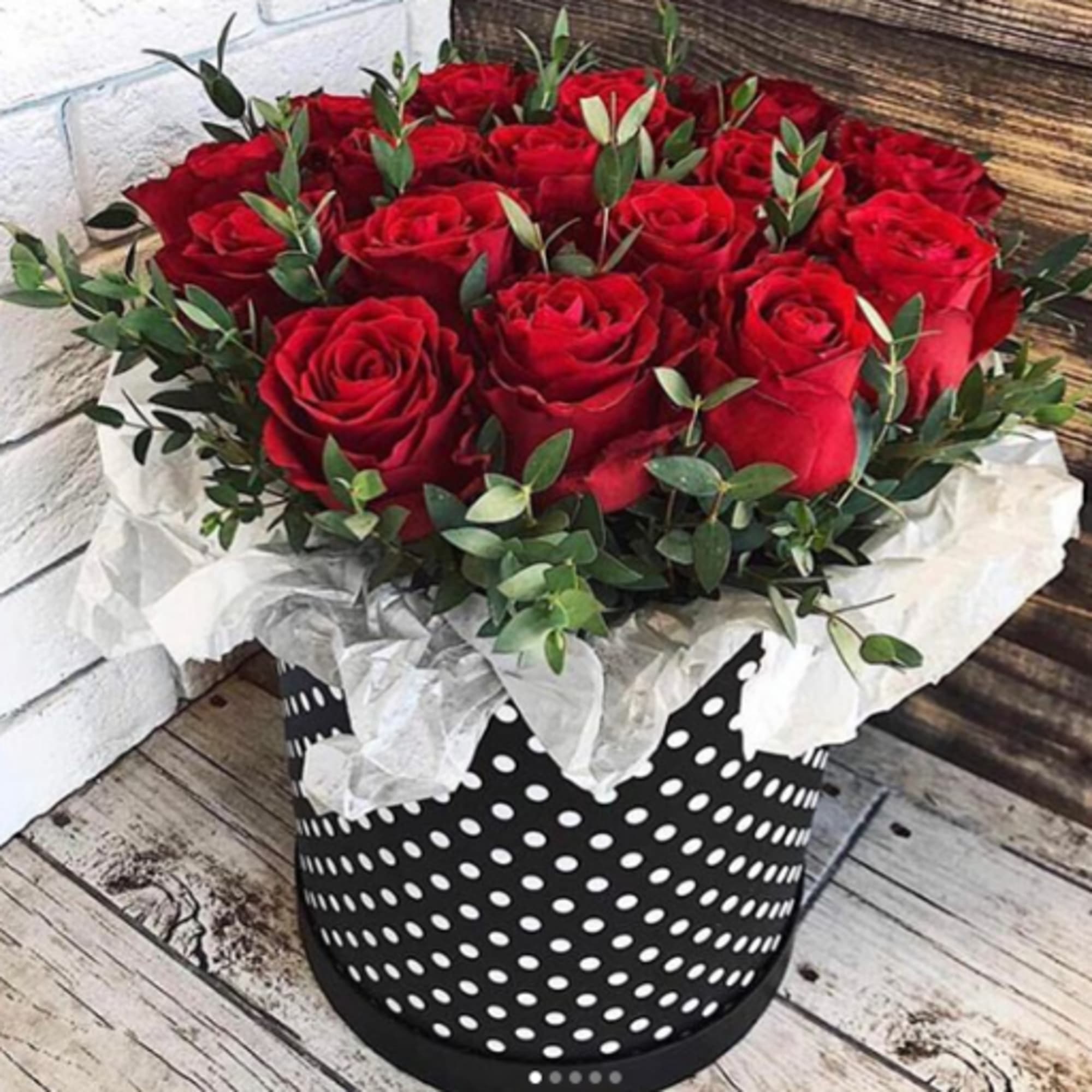 Round box of red roses with greenery in a black polka dot container lined with white tissue paper