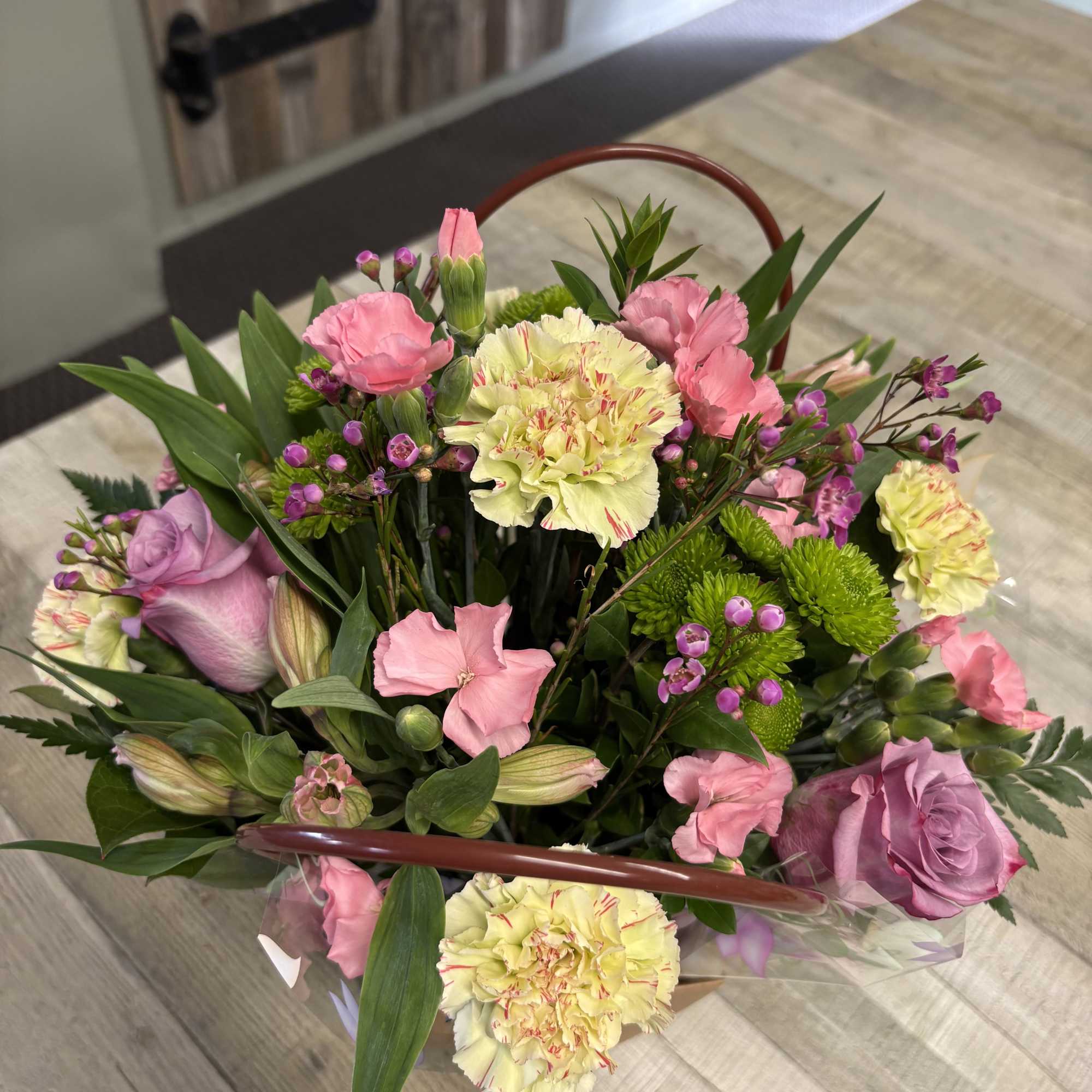 Handheld bouquet of pink and yellow flowers with greenery