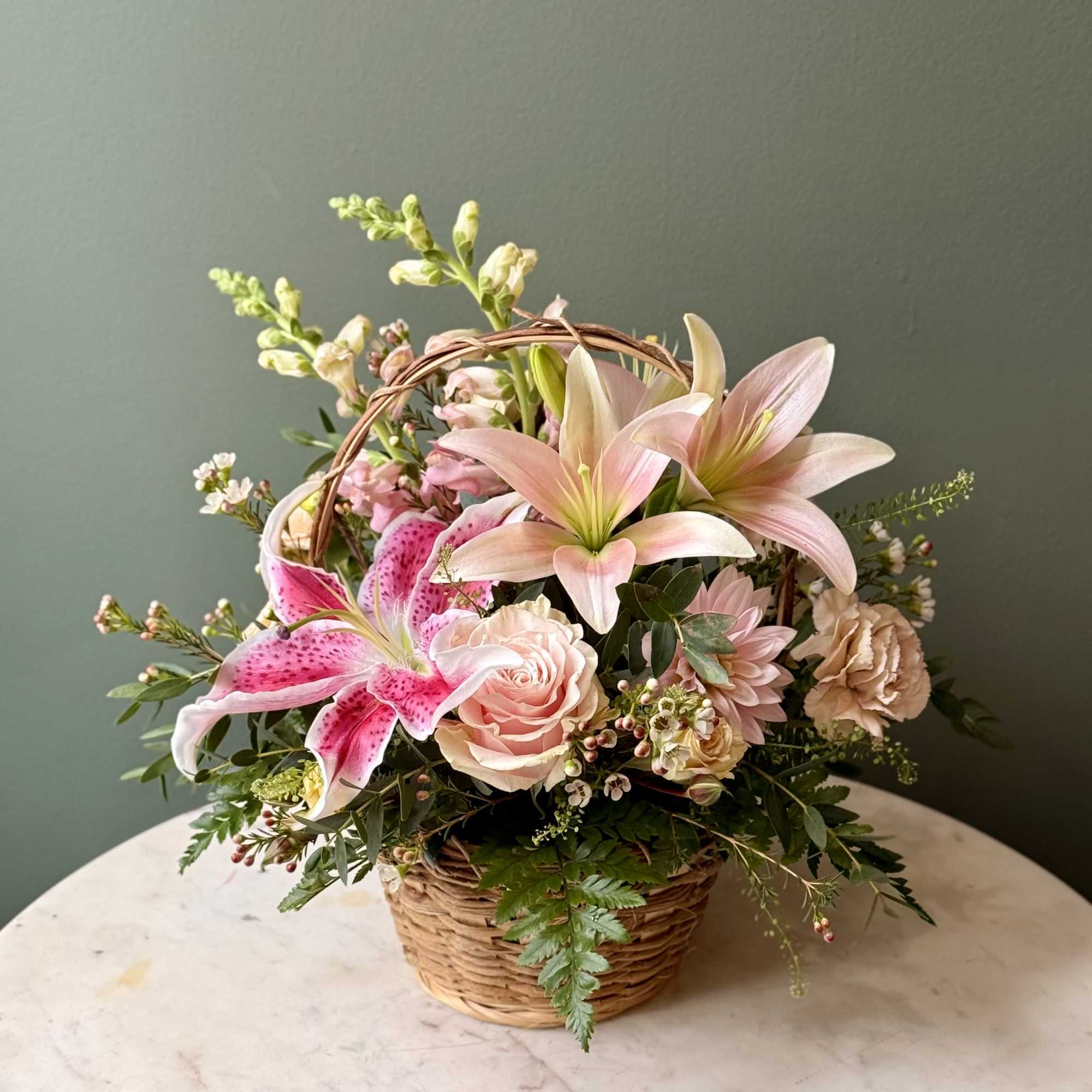 Pink lilies, roses, and mixed blooms arranged in a small wicker basket