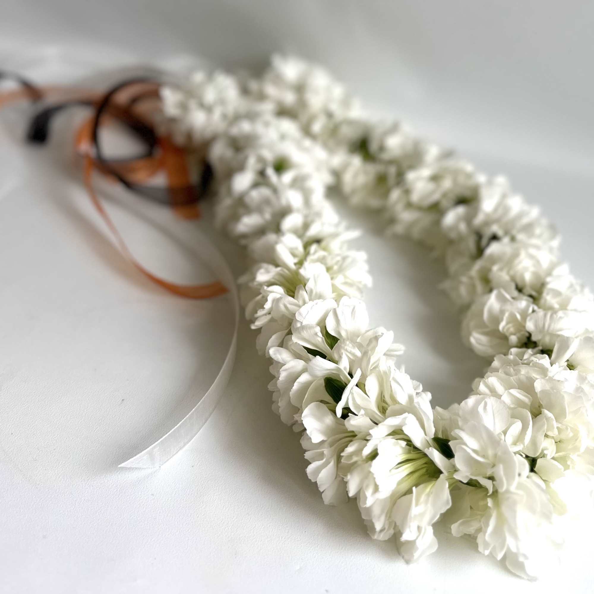 White flower lei with orange and black ribbons