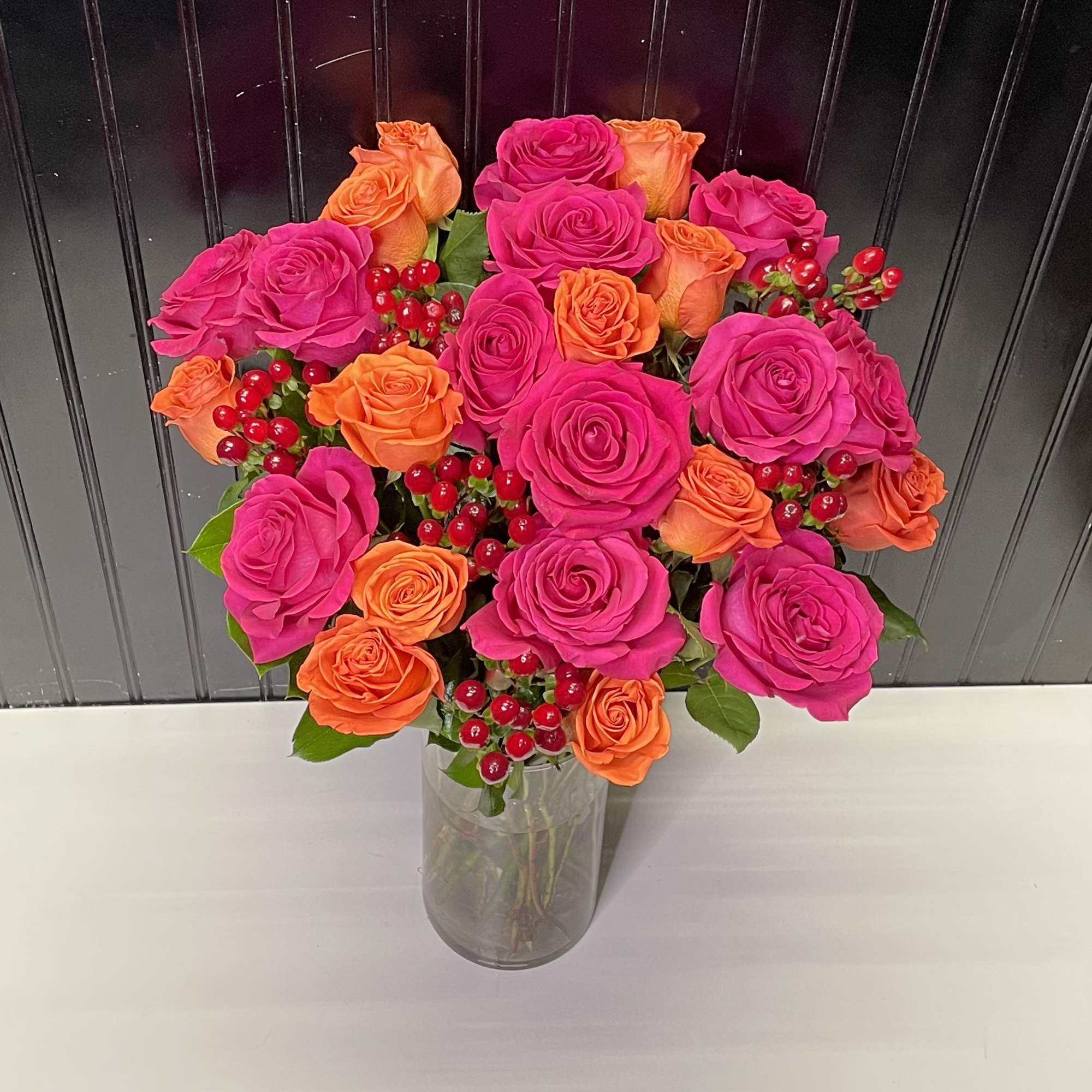 Tall vase of hot pink and orange roses accented with red berries