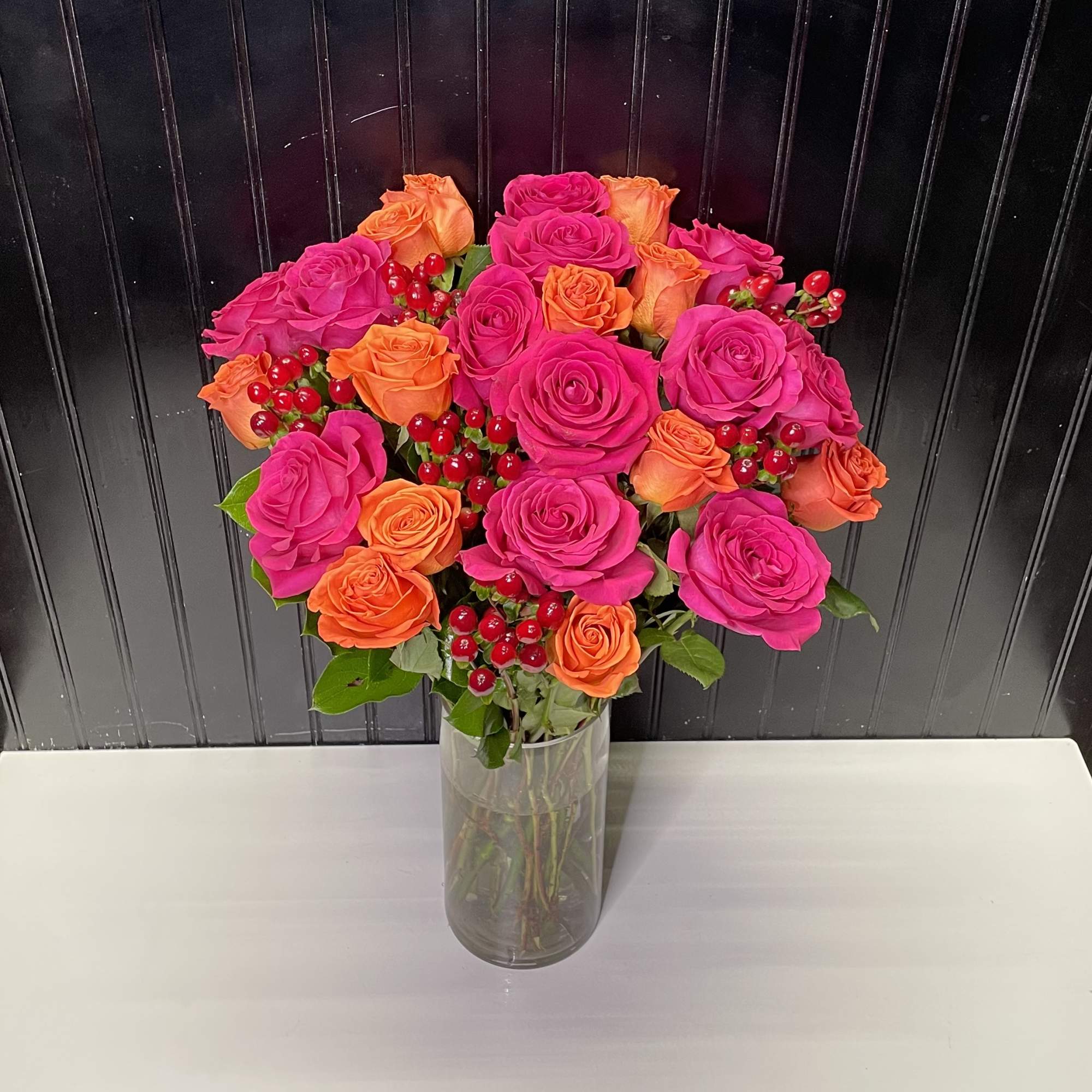 Tall vase of hot pink and orange roses accented with red berries