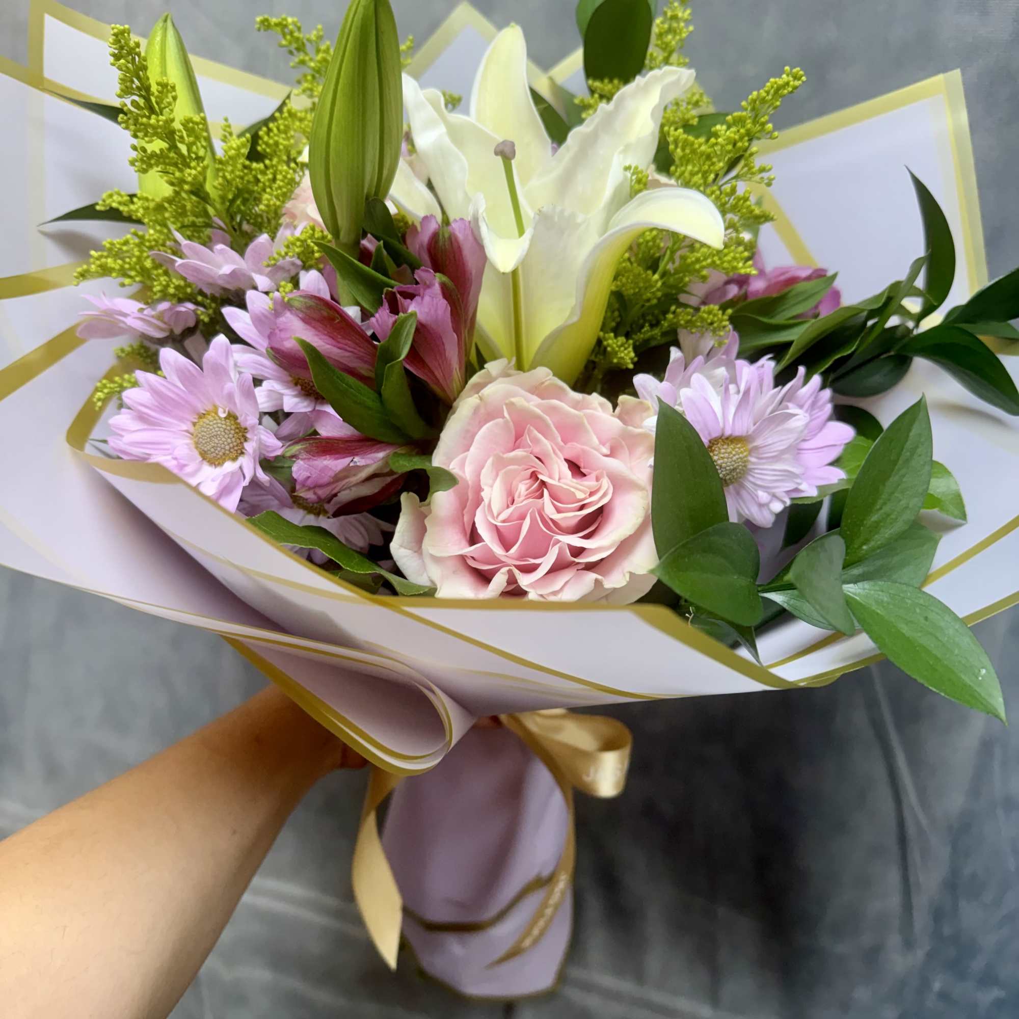Bouquet of pink and white flowers wrapped in white paper with gold trim