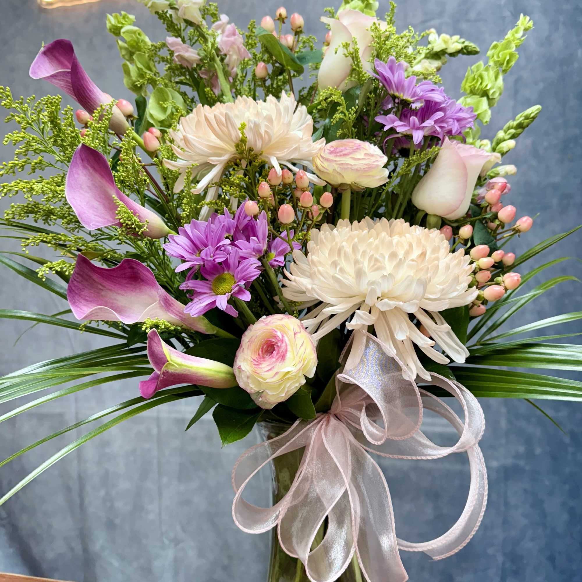 Mixed bouquet with pink calla lilies, white chrysanthemums, and purple daisies in a glass vase