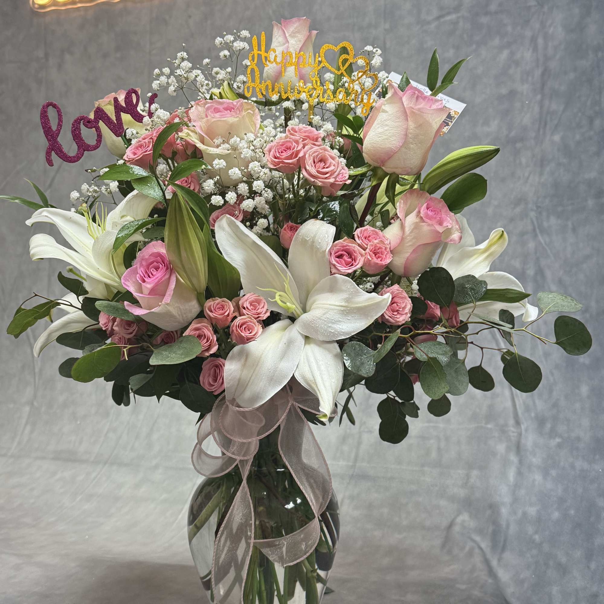 Pink roses and white lilies in a glass vase with anniversary picks