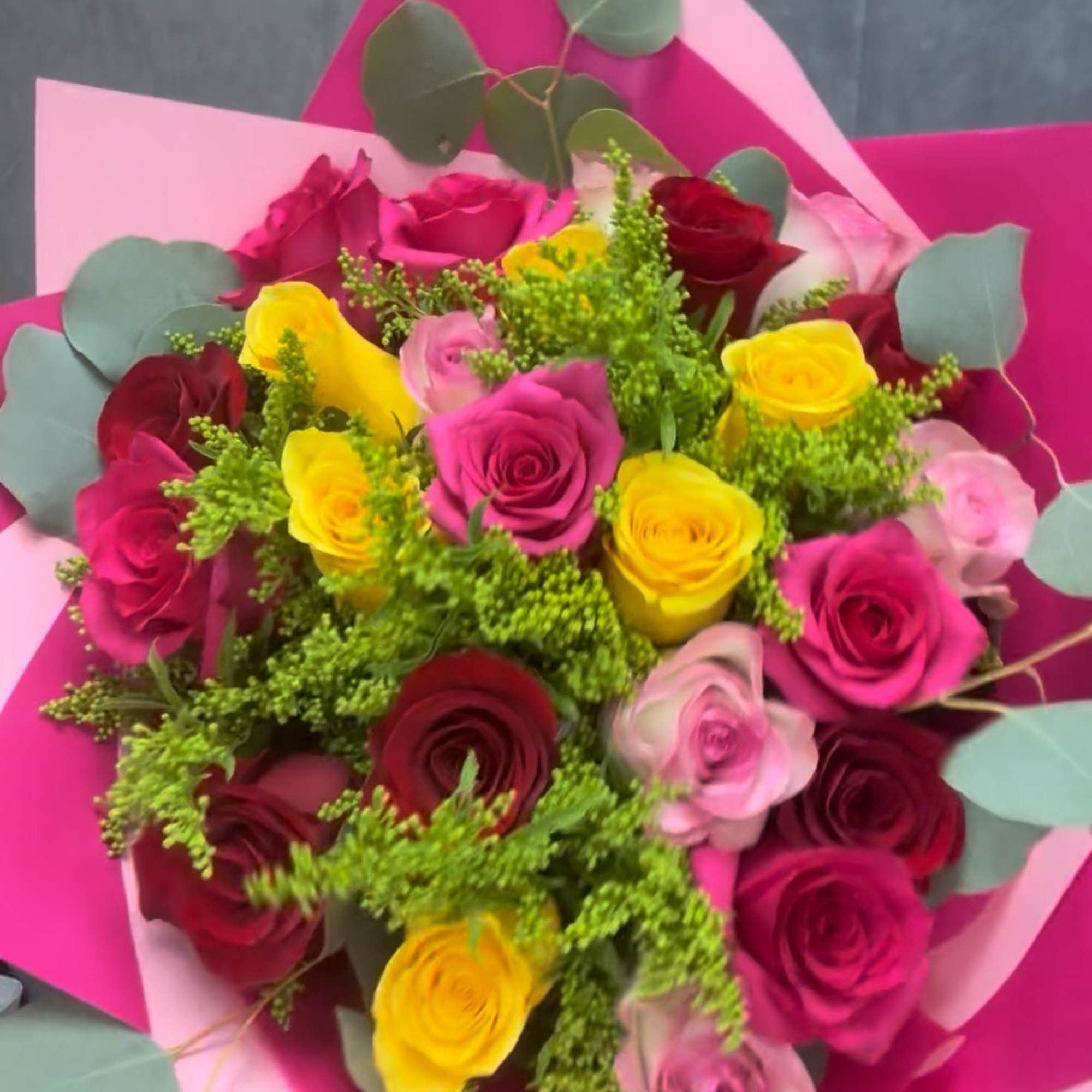 Bouquet of pink, red, and yellow roses wrapped in bright pink paper