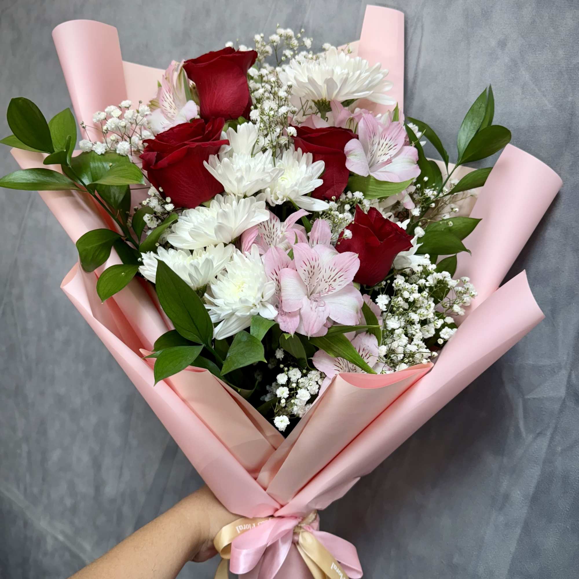 Bouquet of red roses, white daisies, and pink flowers wrapped in pink paper