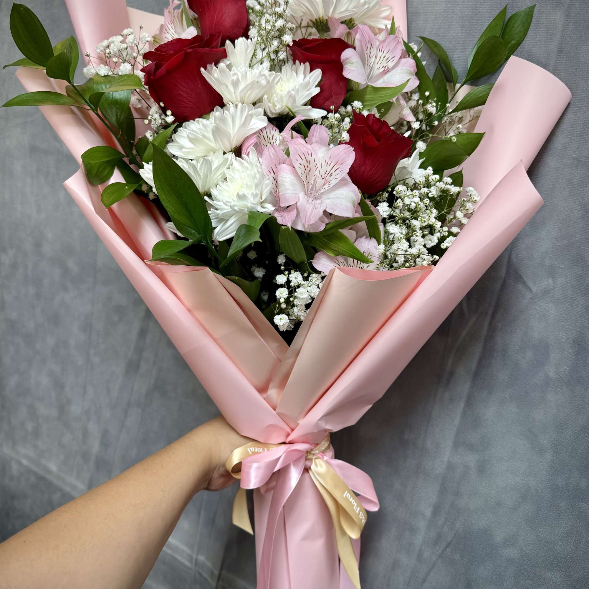 Bouquet of red roses, white daisies, and pink alstroemeria wrapped in pink paper
