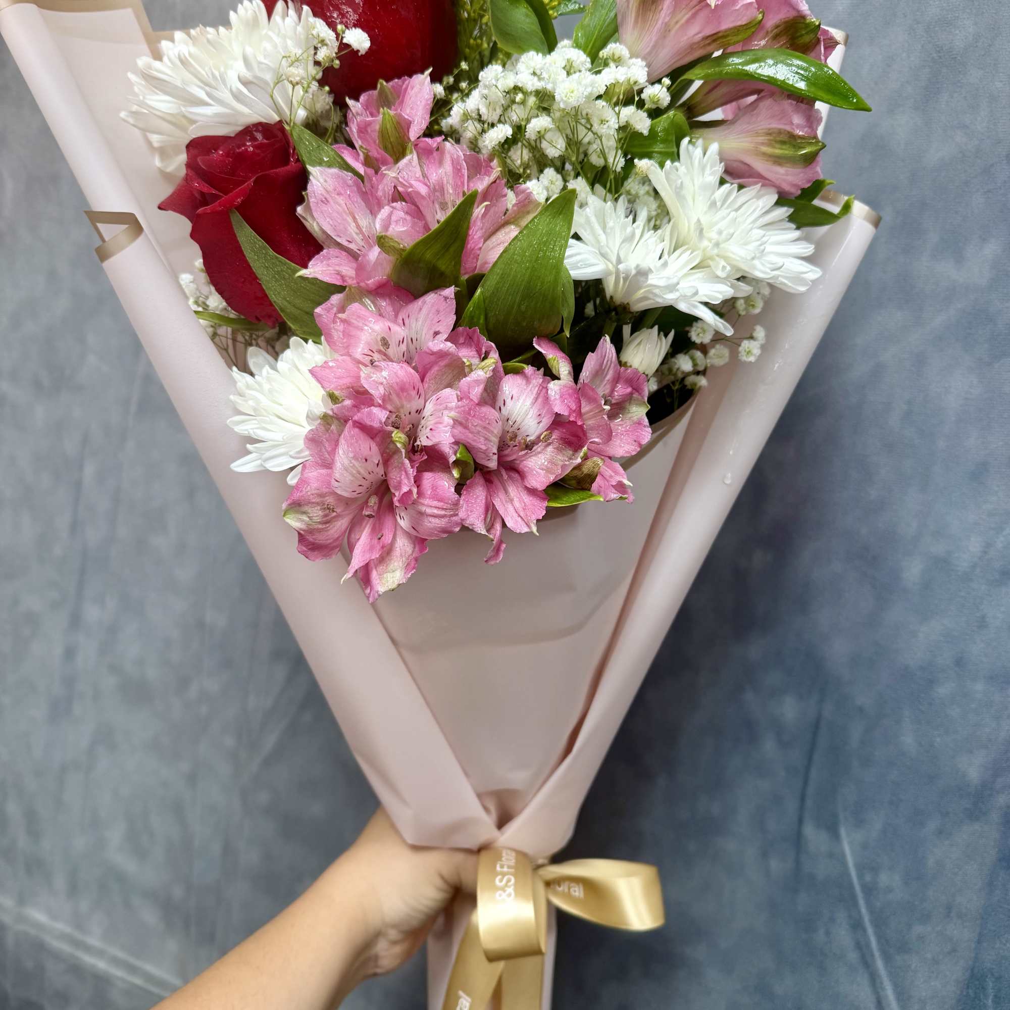 Bouquet of red roses, pink alstroemeria, and white daisies wrapped in blush paper
