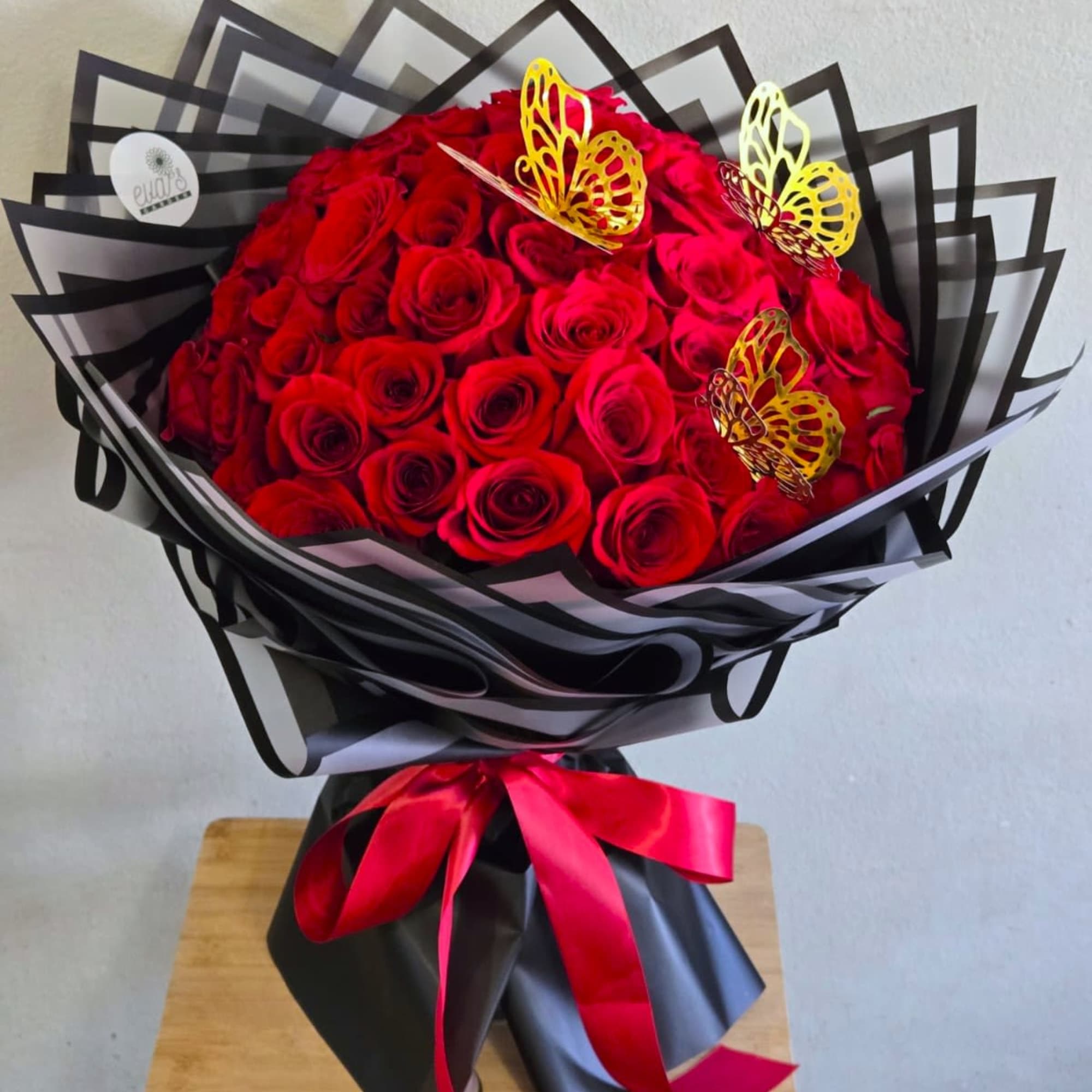 Bouquet of red roses wrapped in black paper with a red ribbon and butterfly accents