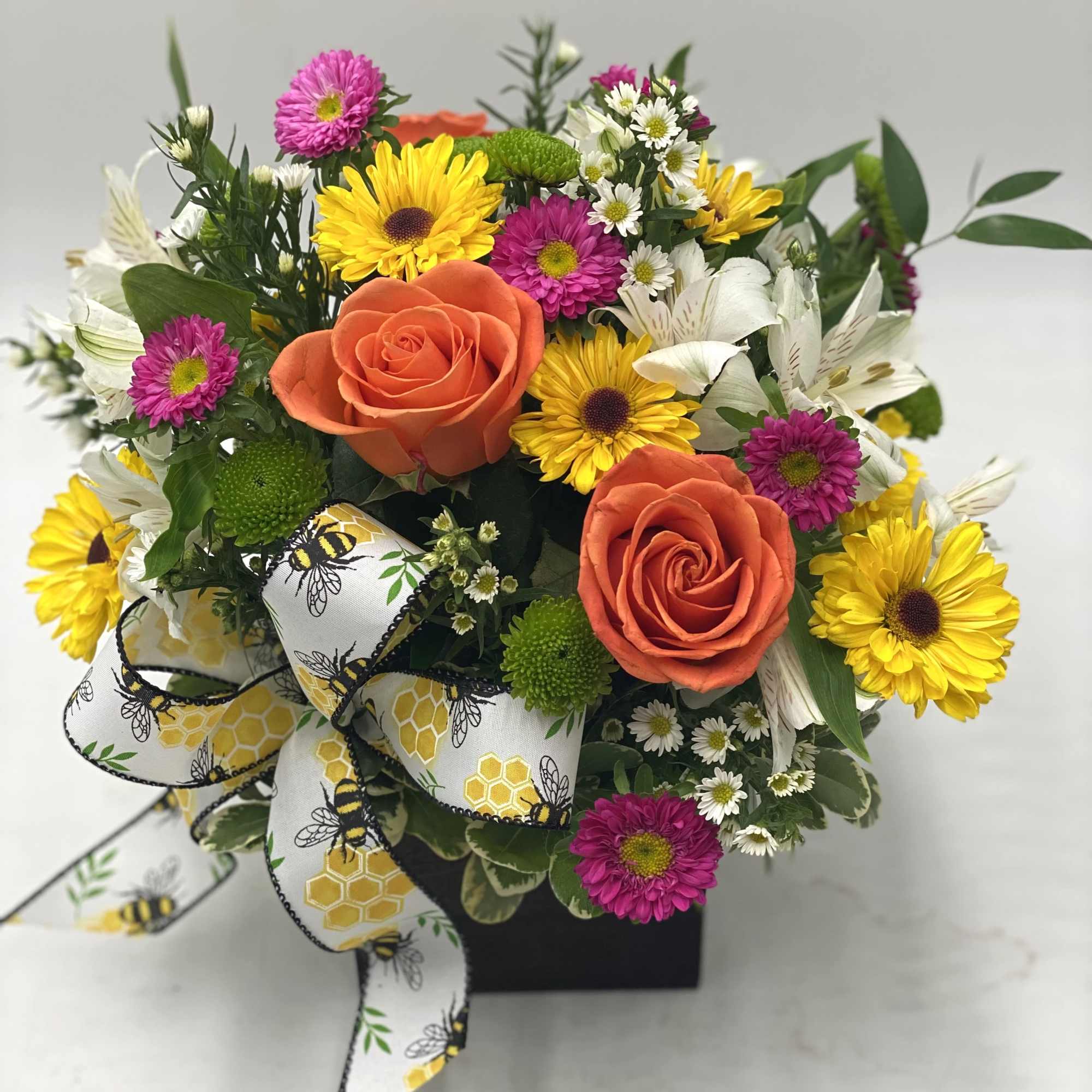 Bouquet of orange roses, yellow daisies, and purple mums with a bee-patterned ribbon