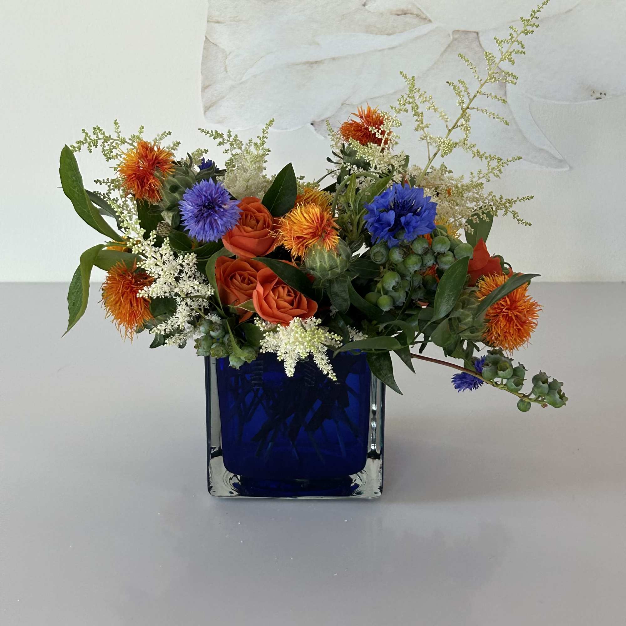 Mixed bouquet of orange and blue flowers in a cobalt glass vase