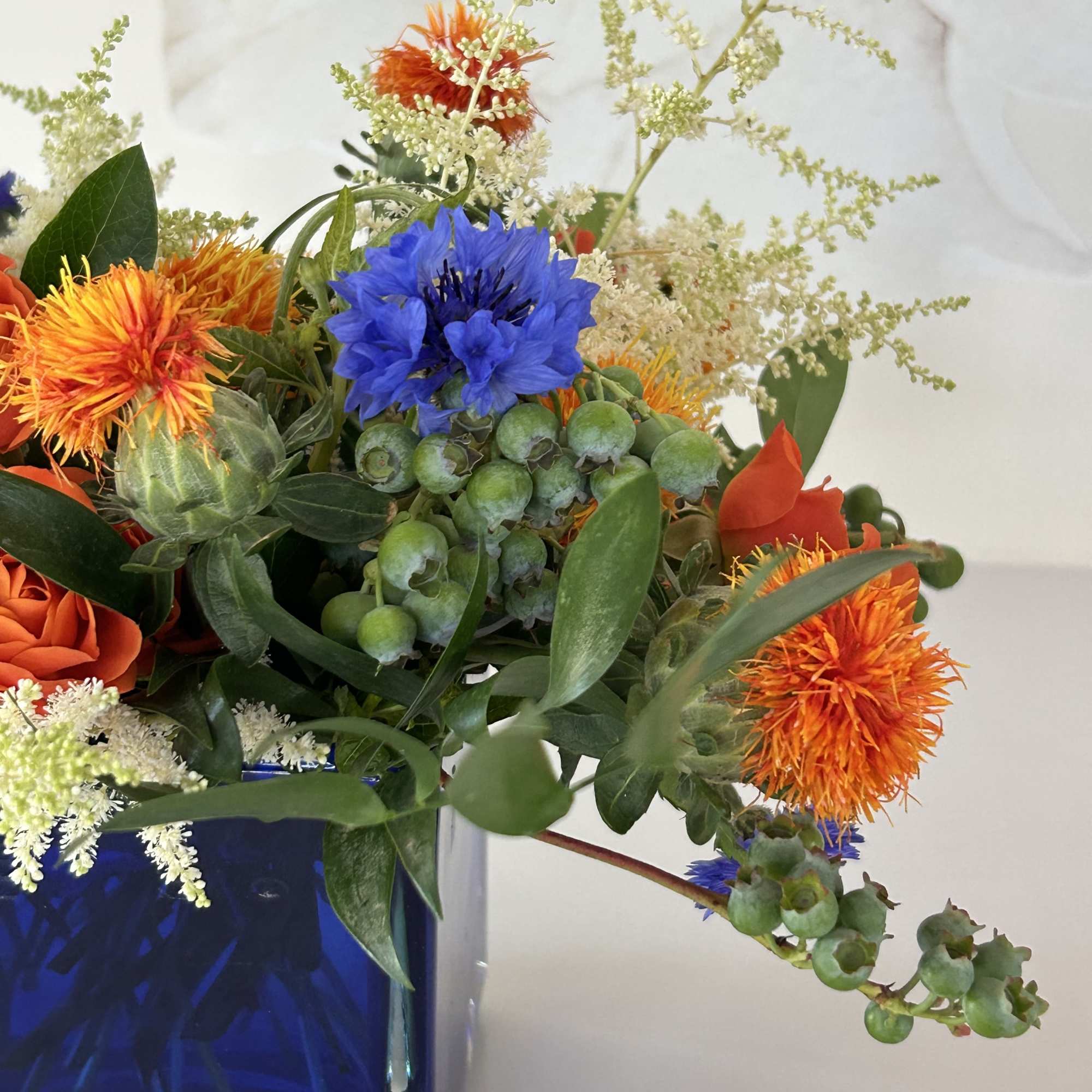 Mixed bouquet in a blue glass vase with orange and blue blooms