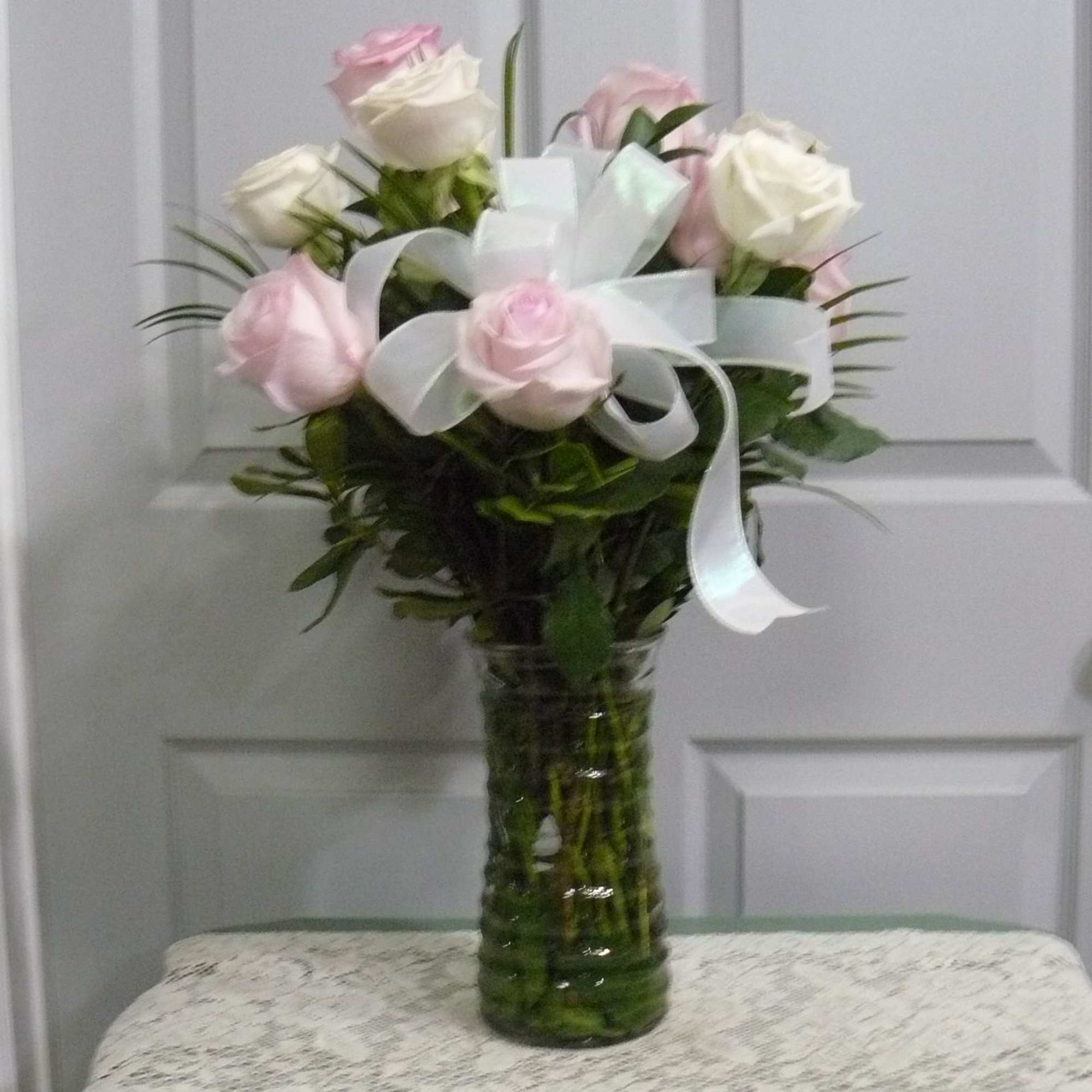 Pink and white roses arranged in a tall glass vase with a white ribbon