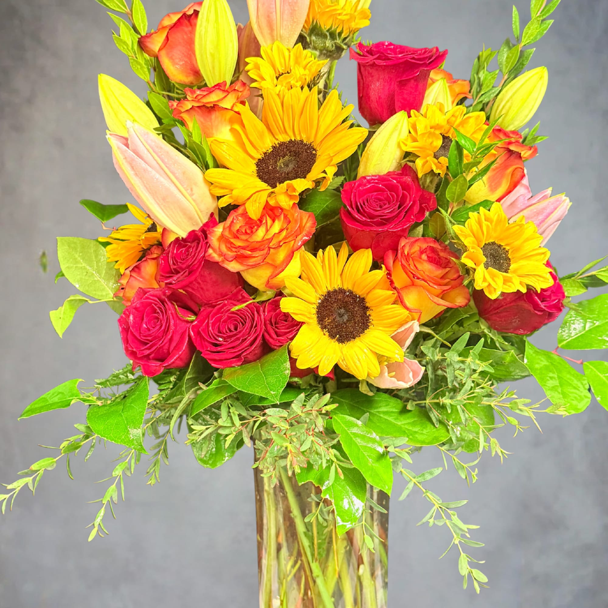 Mixed bouquet of roses, sunflowers, and lilies in a glass vase