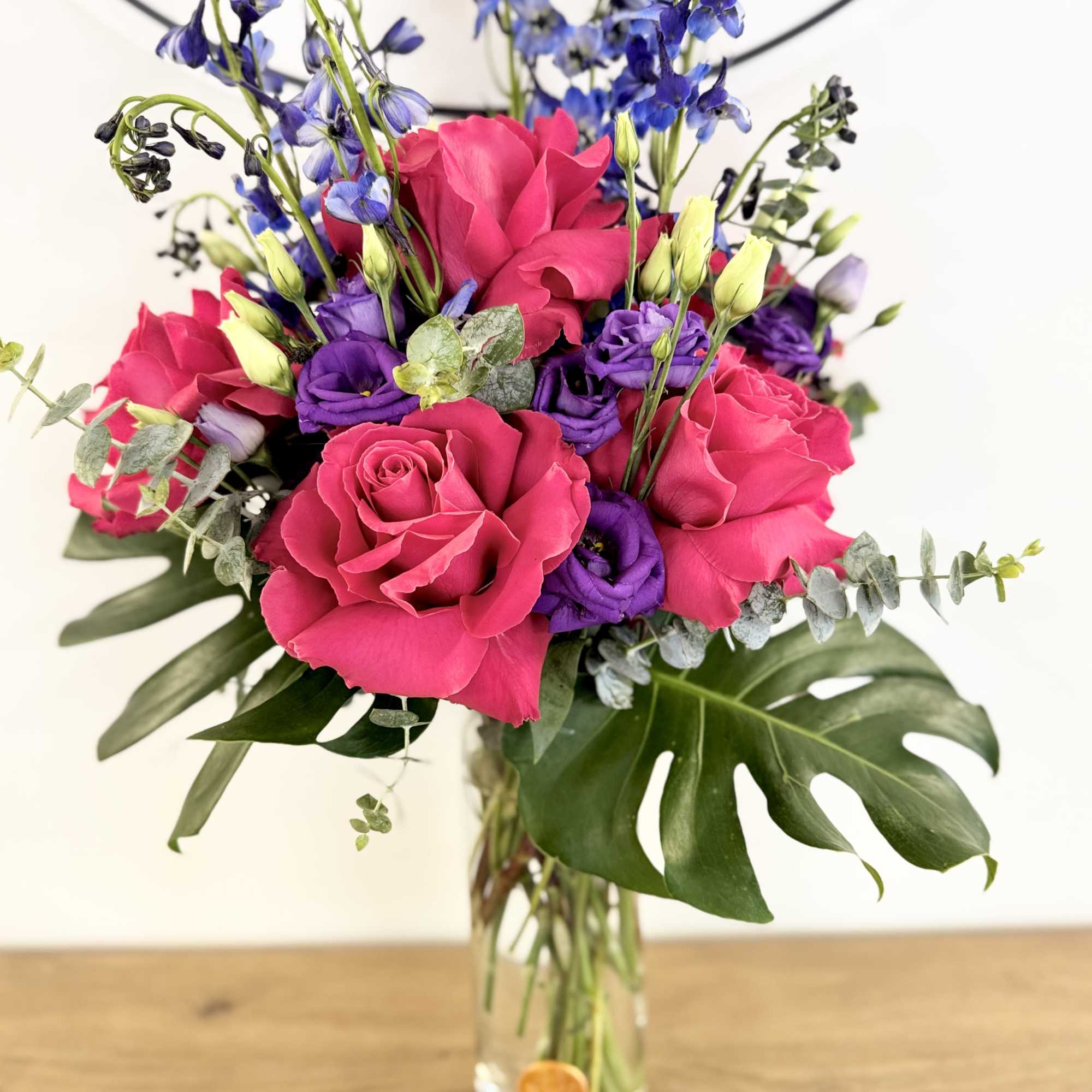 Featuring monstera leaves, delphinium, roses, and eucalyptus, this blue, green, and red