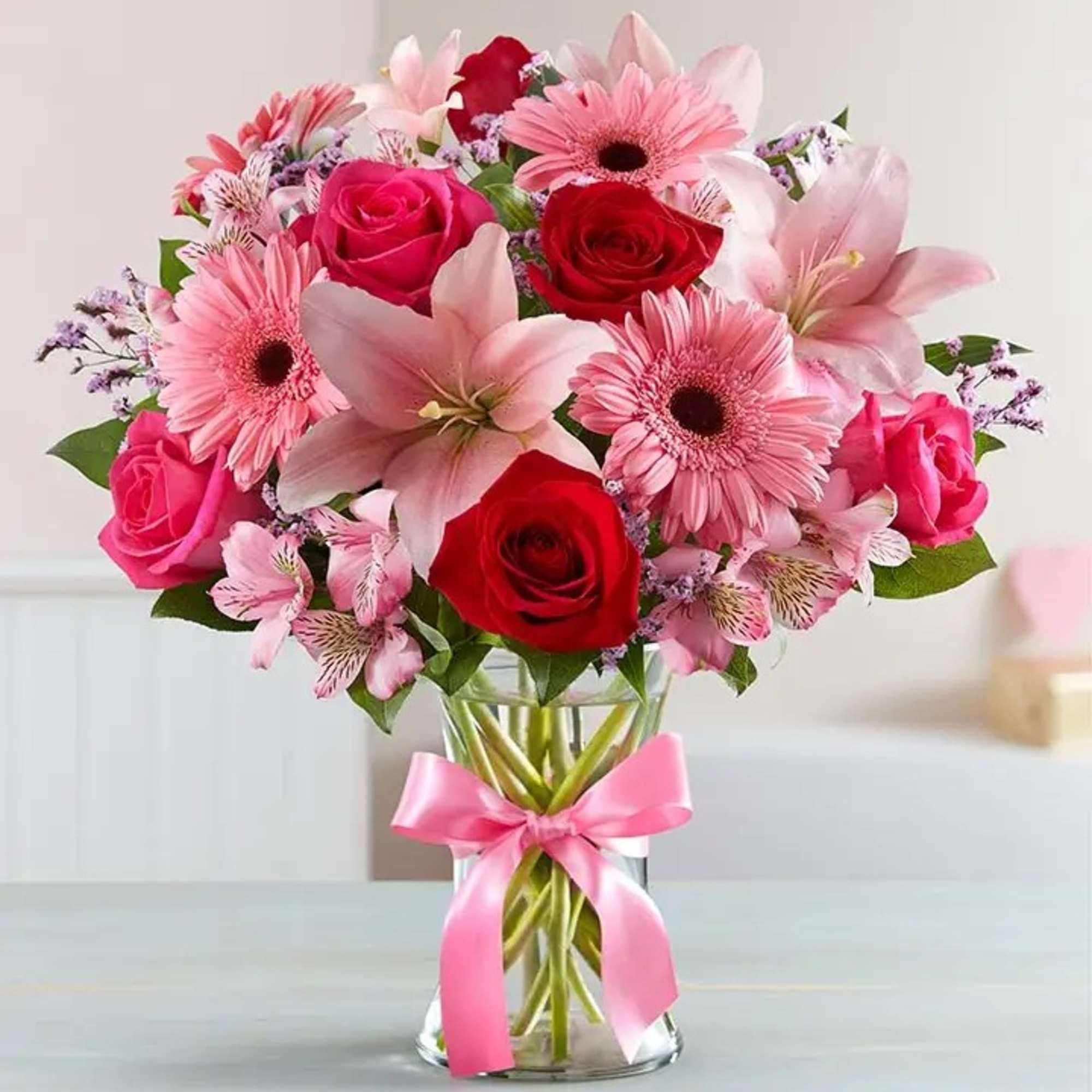 Pink and red mixed bouquet in a clear glass vase with a pink ribbon