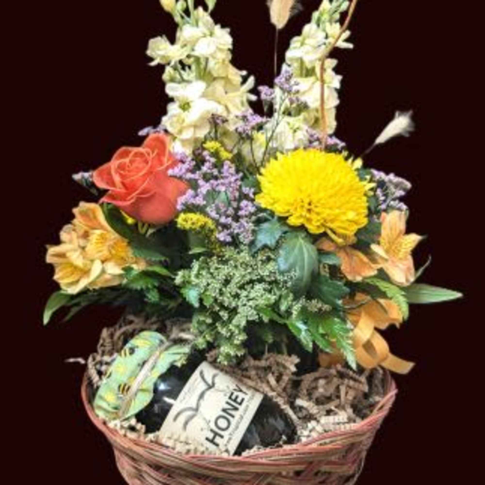 Basket arrangement with mixed flowers and a honey gift item