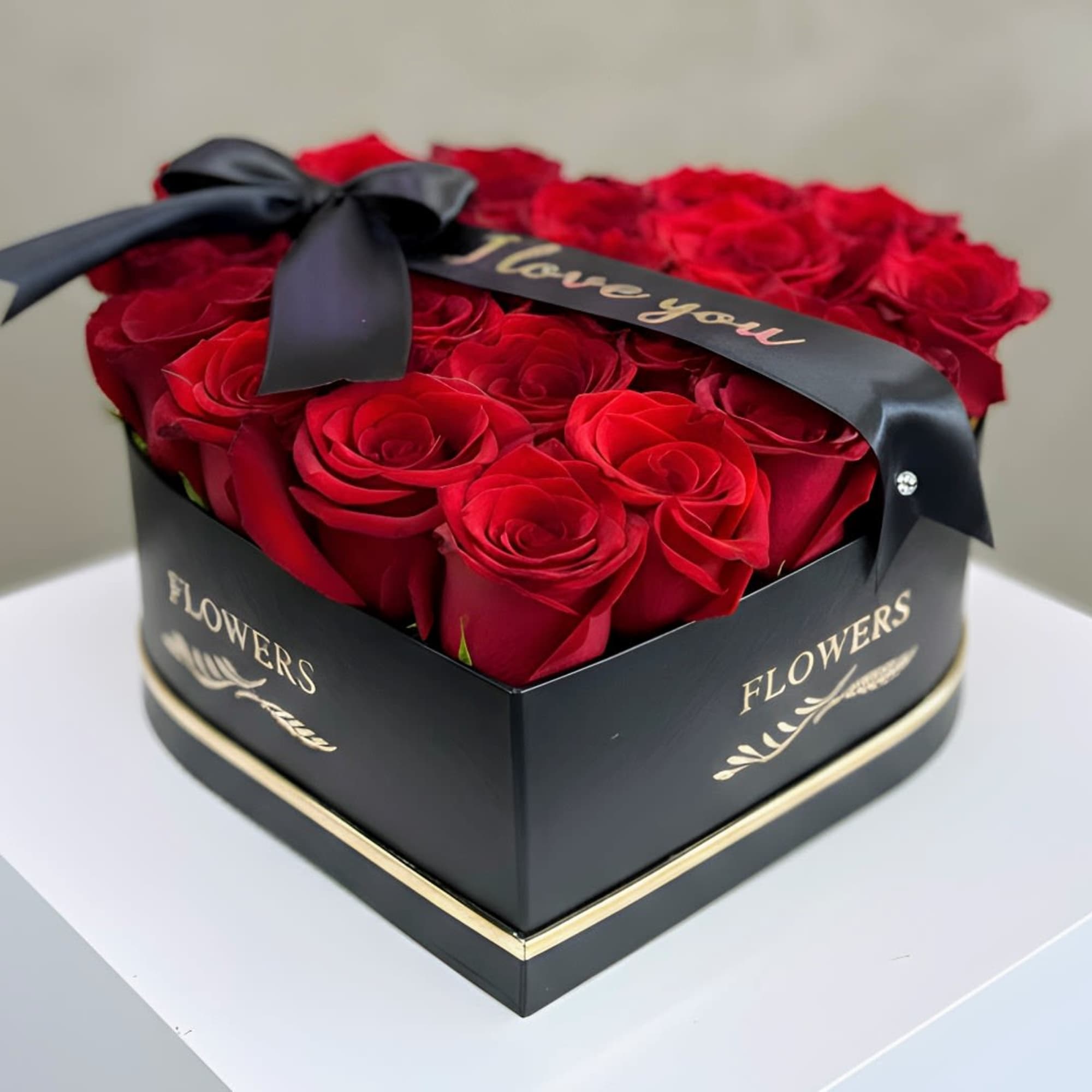 Red roses arranged in a black heart-shaped box with a ribbon