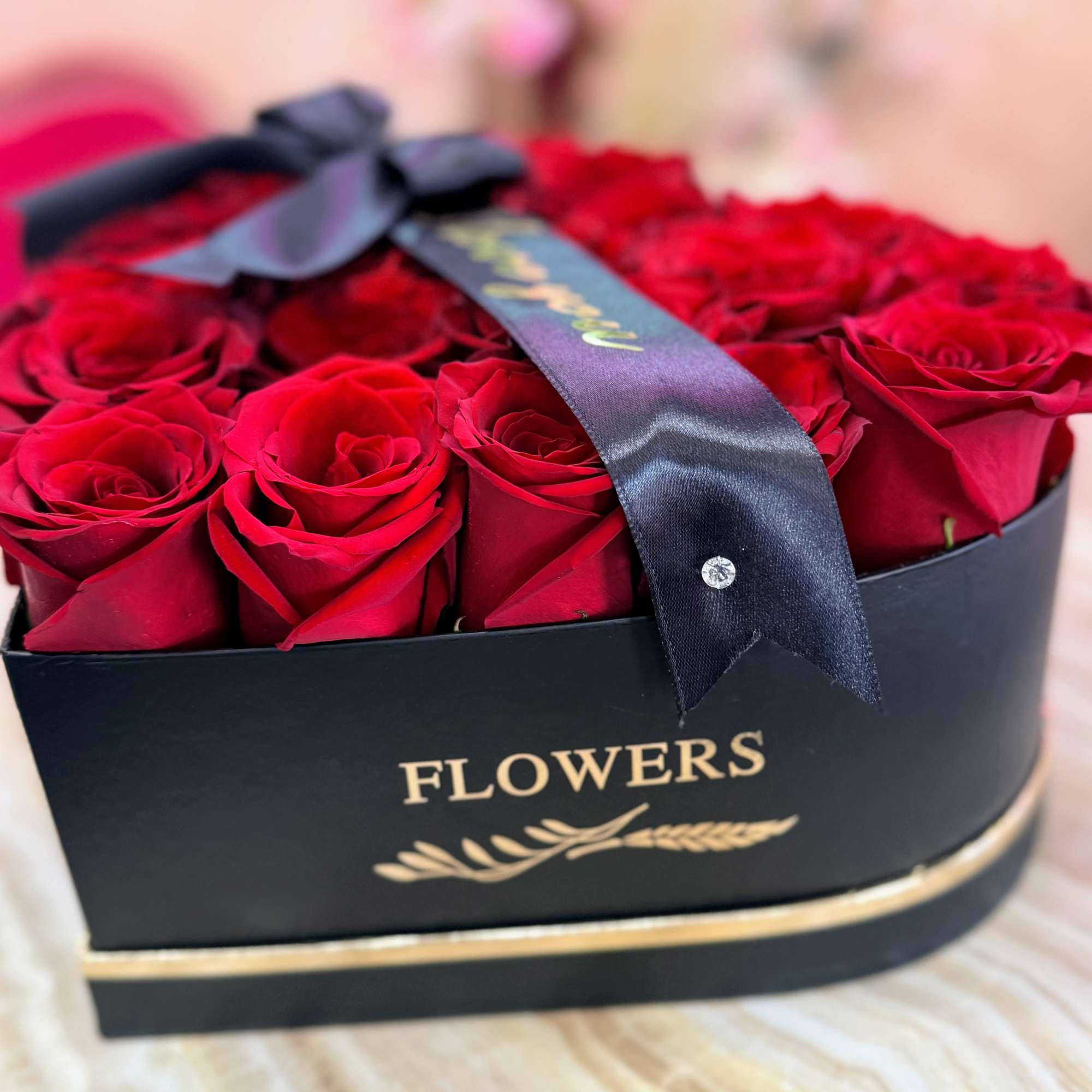 Red roses arranged in a black heart-shaped box with a ribbon