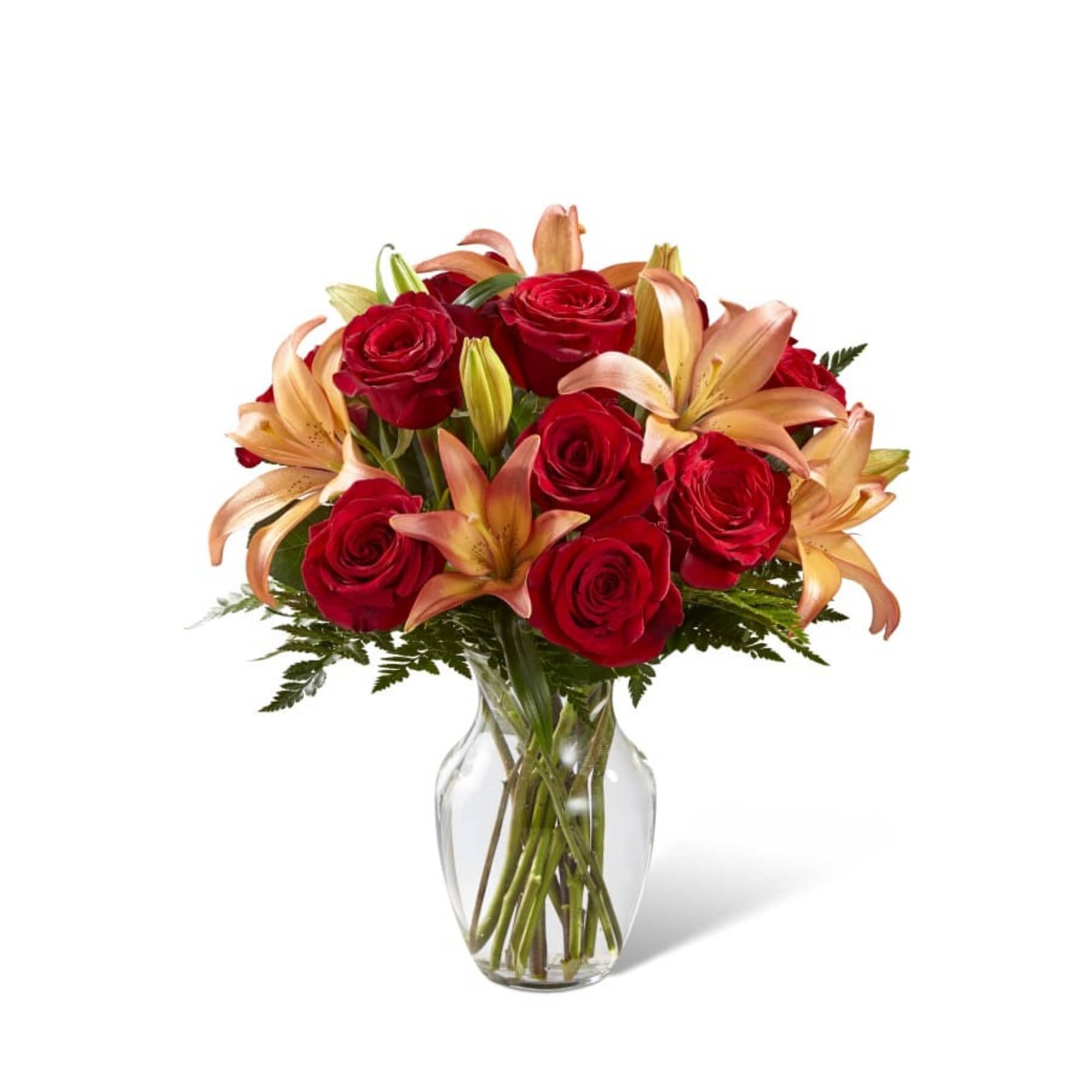 Red roses and peach lilies in a clear glass vase