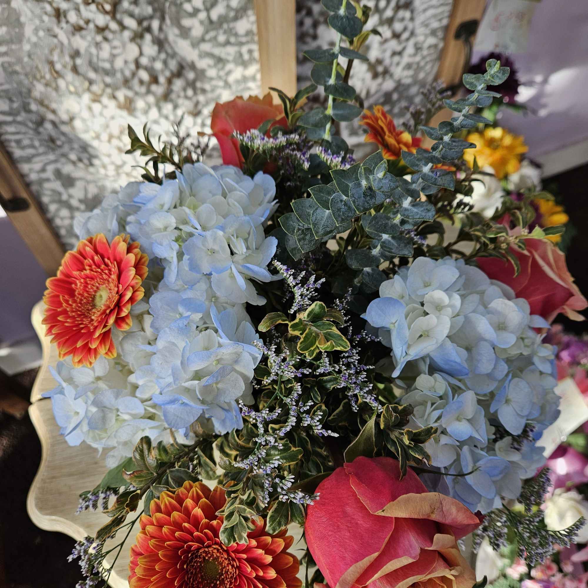 Arrangement of blue hydrangeas, orange gerbera daisies, and pink roses with small filler flowers.