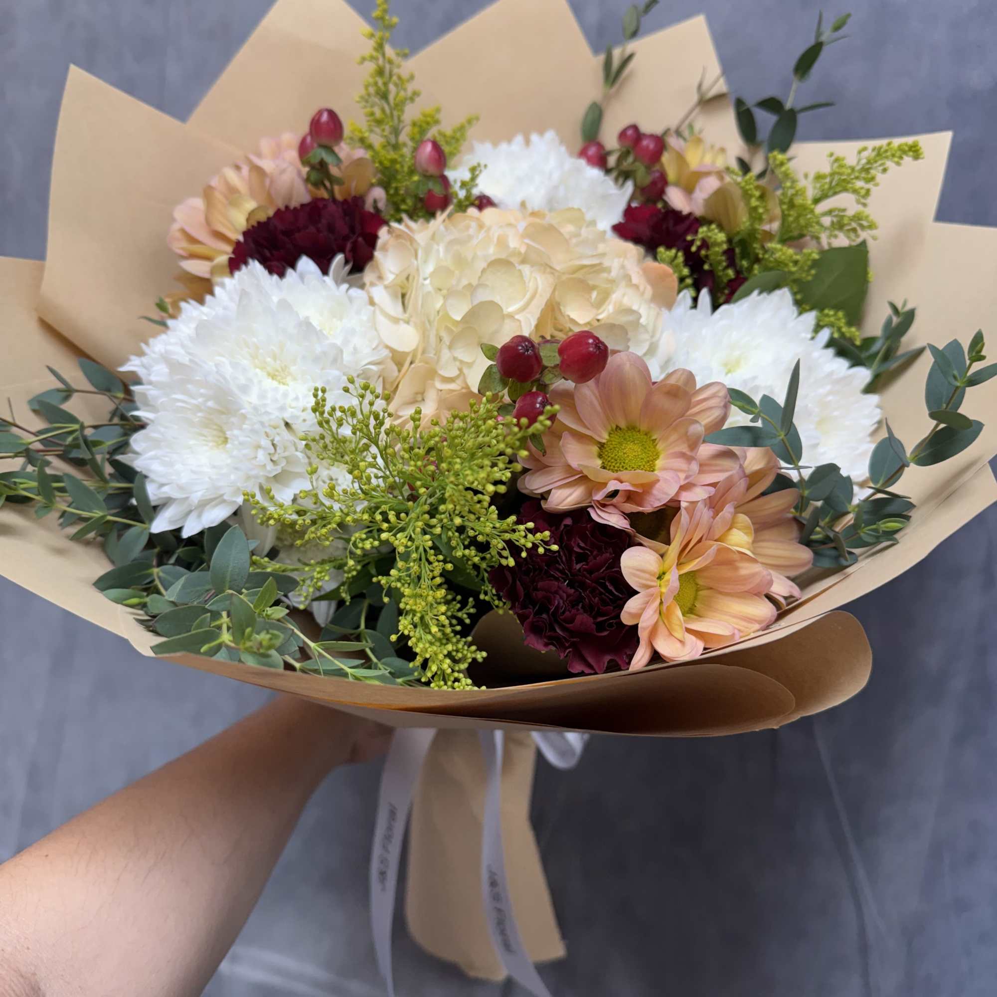 A charming blend of soft peach blooms, creamy hydrangea, white chrysanthemums, burgundy