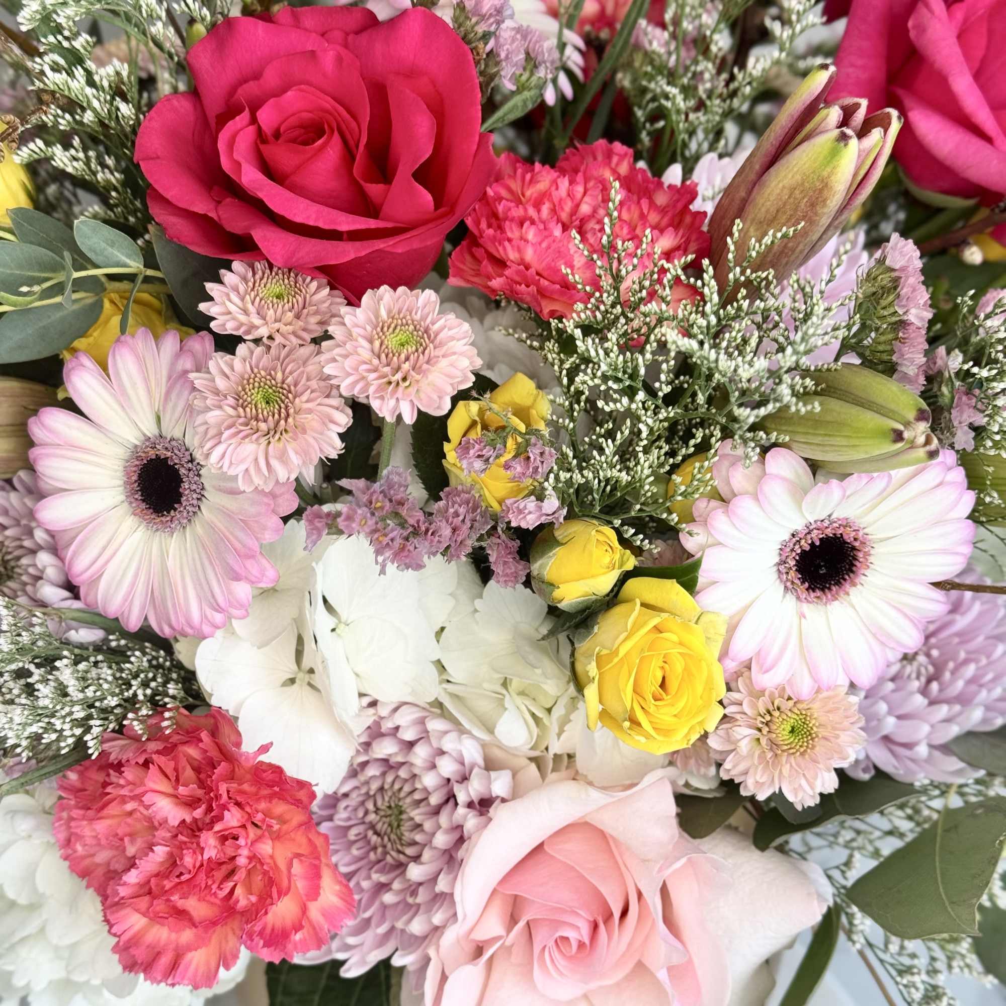 Mixed bouquet of pink roses, gerbera daisies, carnations, chrysanthemums, and white hydrangea in a vase