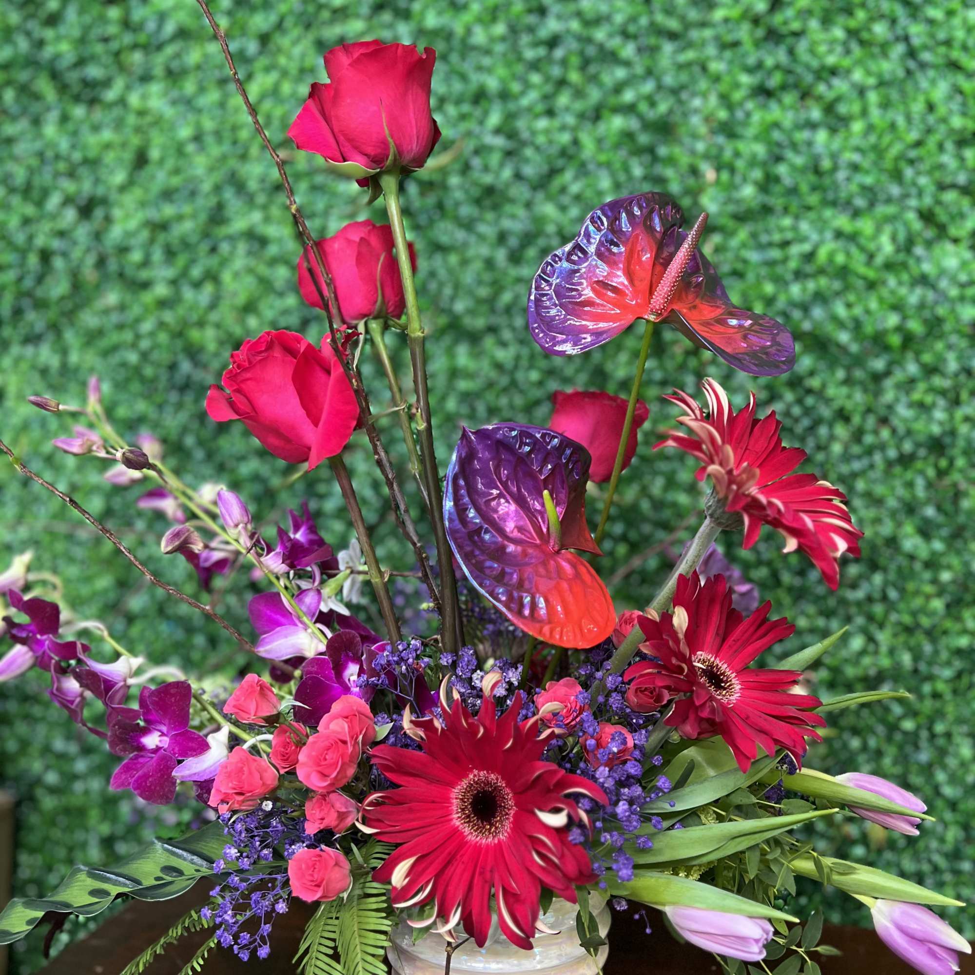 Bright pink roses and red gerbera daisies in a white vase with purple orchids