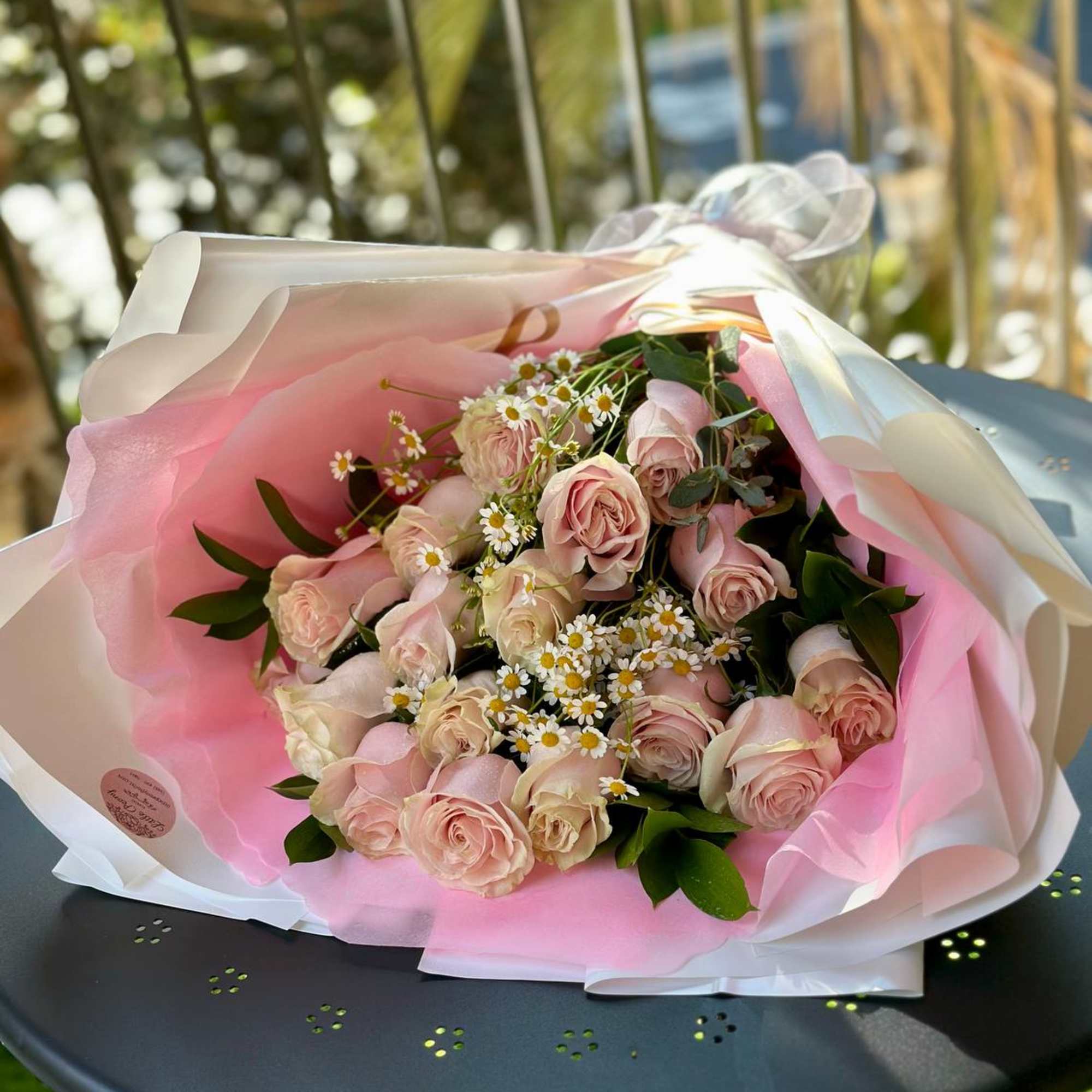 Bouquet of pale pink roses and small white daisies wrapped in pink and white paper
