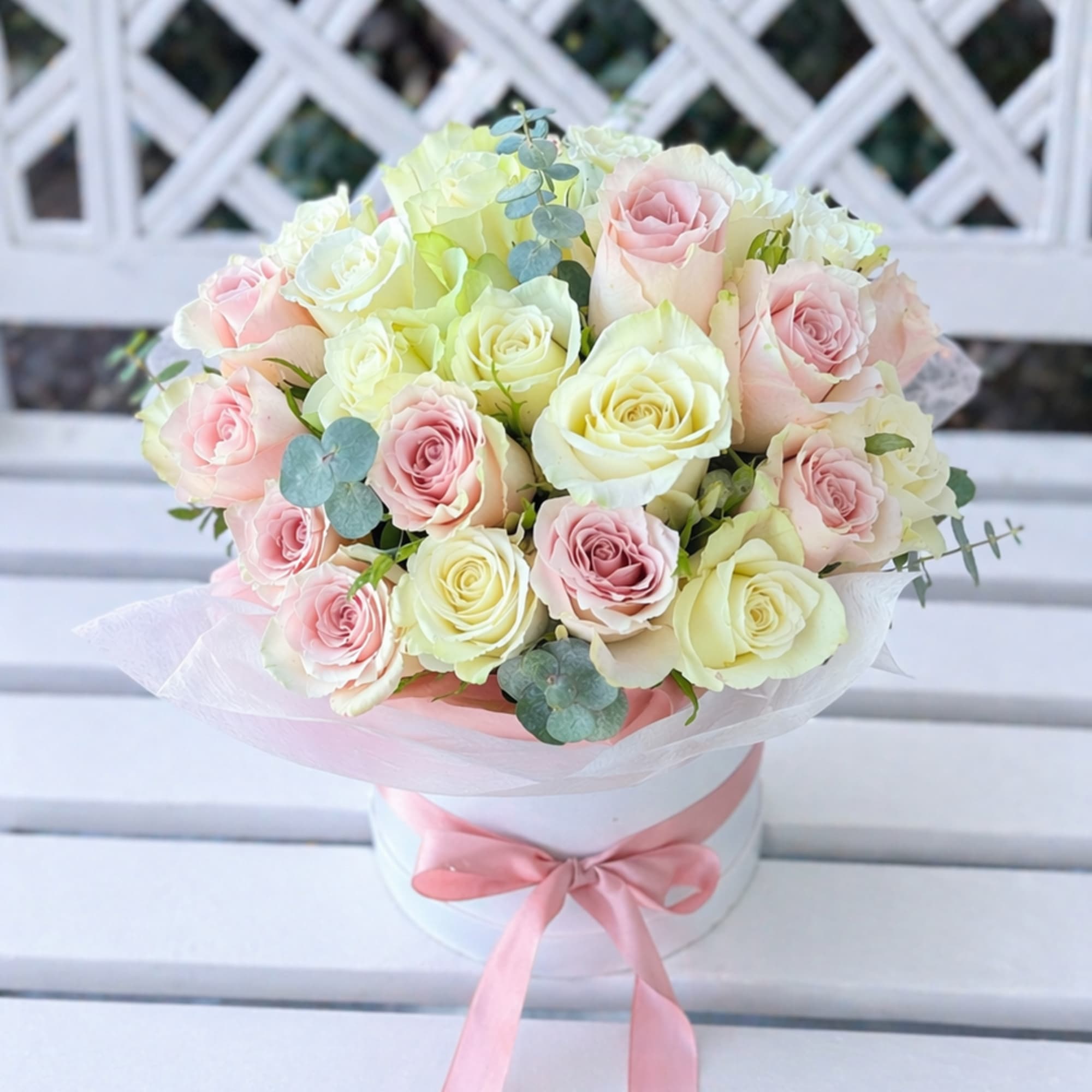 Bouquet of pale pink and cream roses in a white hatbox with a pink ribbon