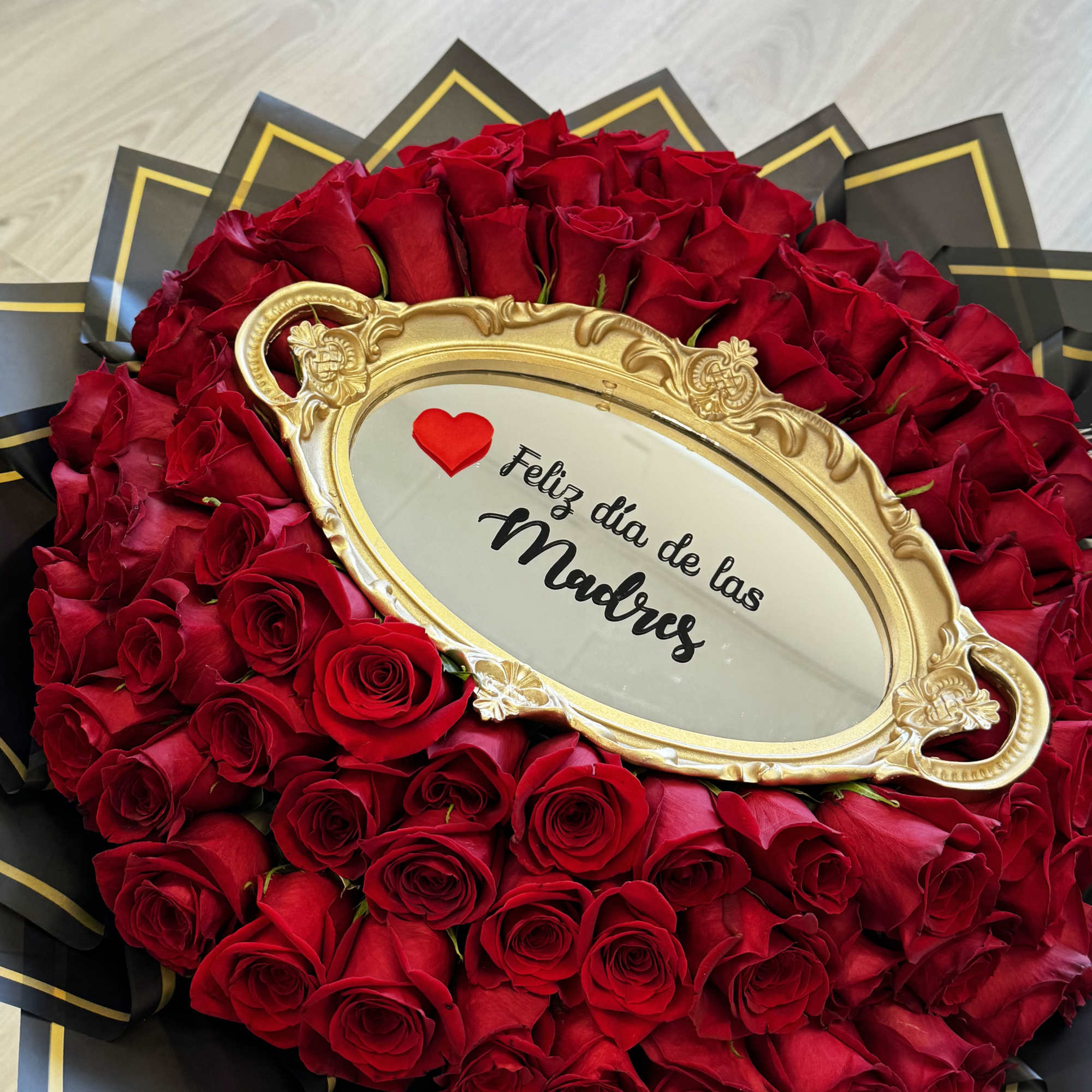 Heart-shaped bouquet of red roses with a gold frame reading "Feliz dia de las Madres"