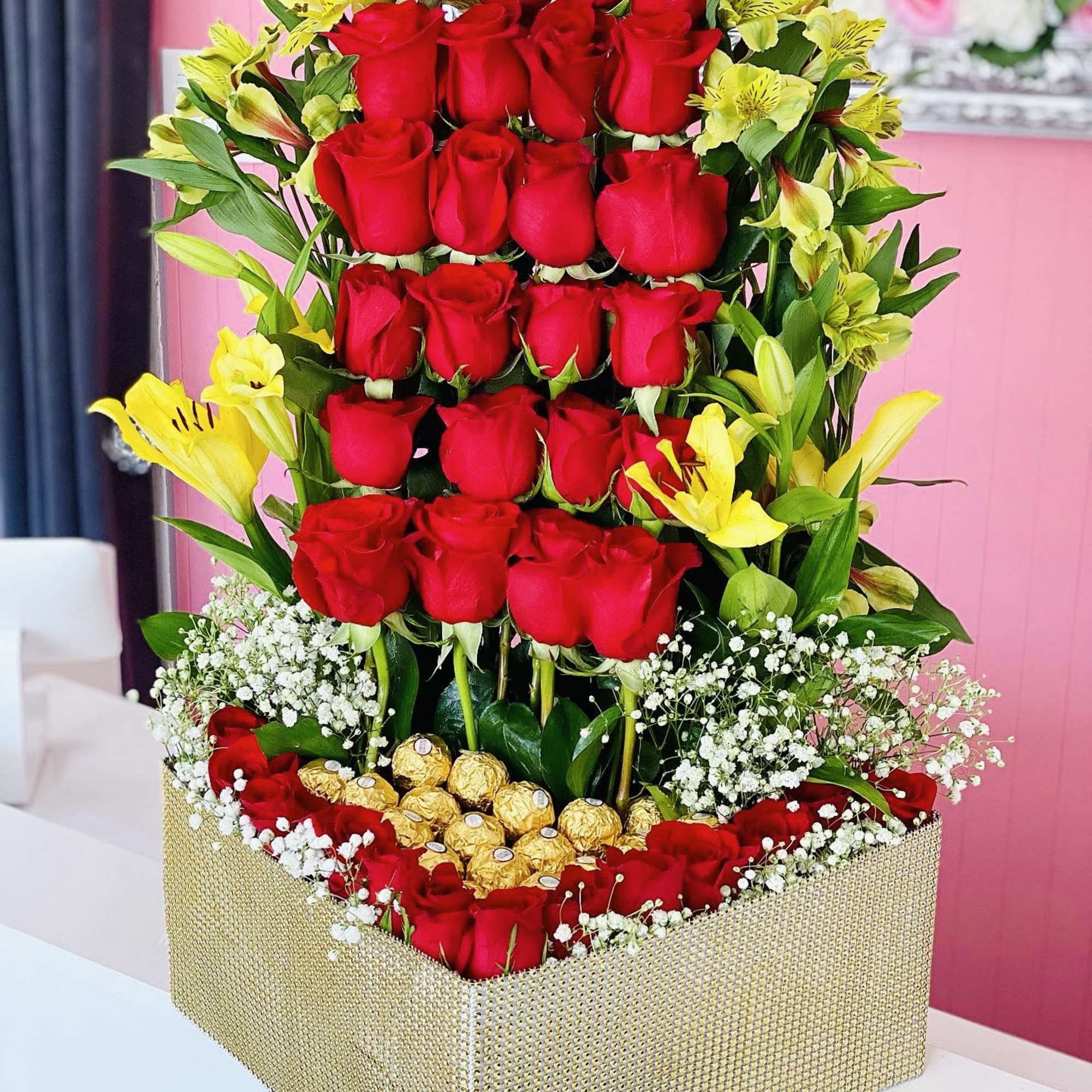 Tall box arrangement of red roses with yellow lilies and gold chocolates
