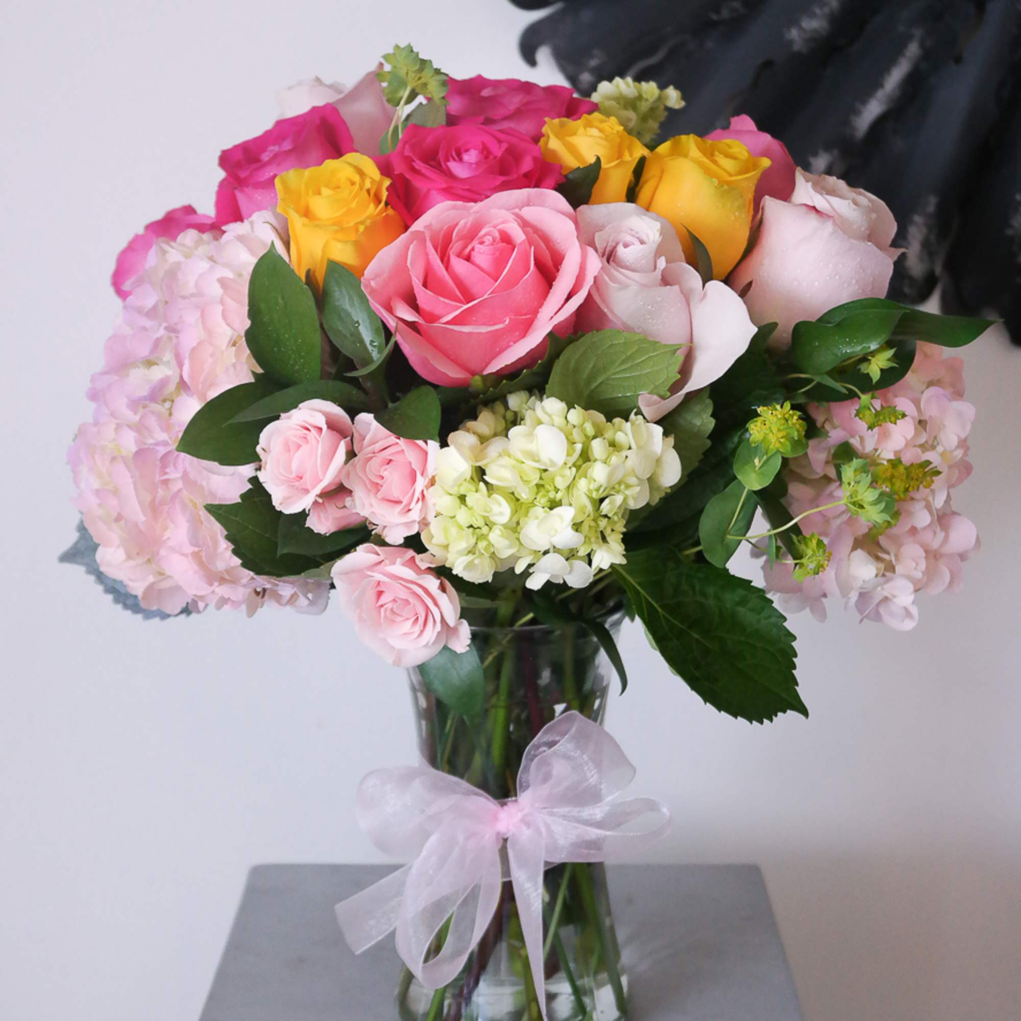 Bouquet of pink, yellow, and white roses in a glass vase with a ribbon