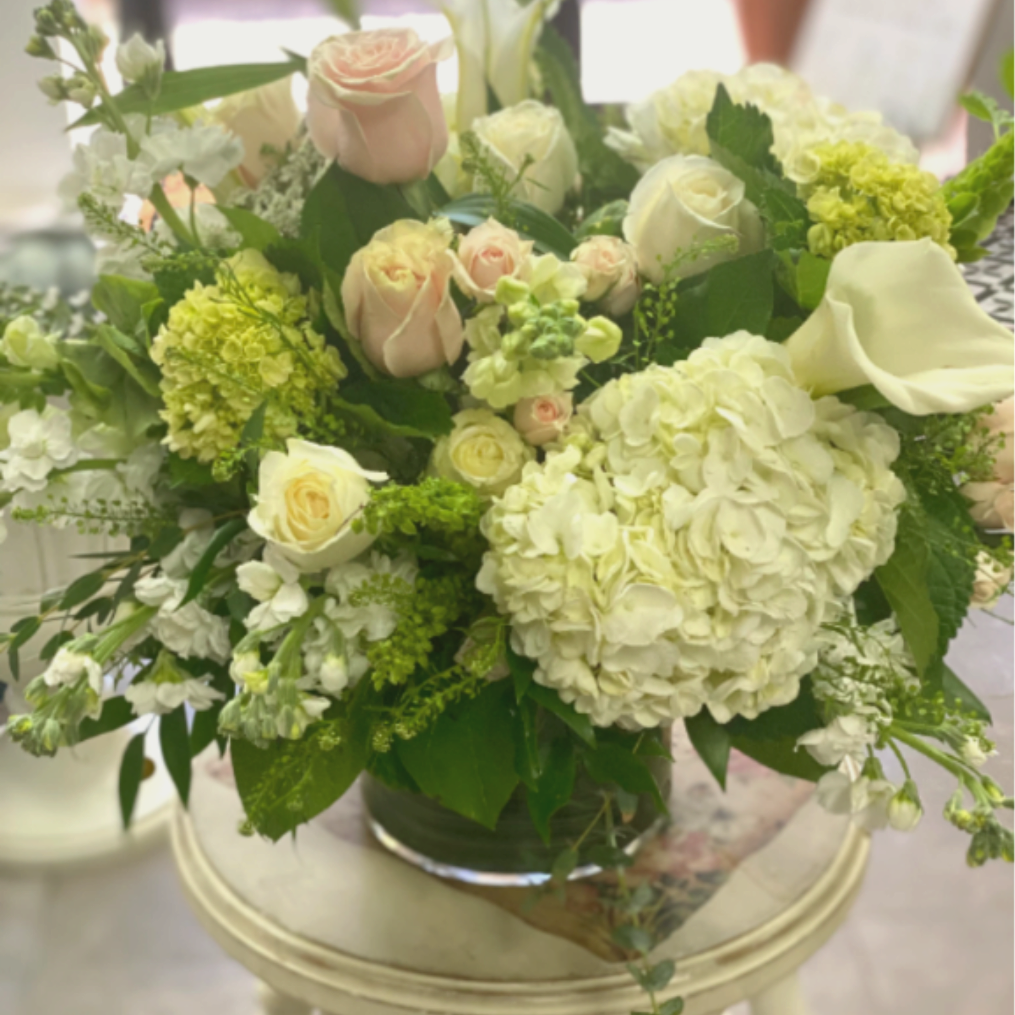 Mixed bouquet of pale roses, hydrangeas, and white calla lilies in a glass vase