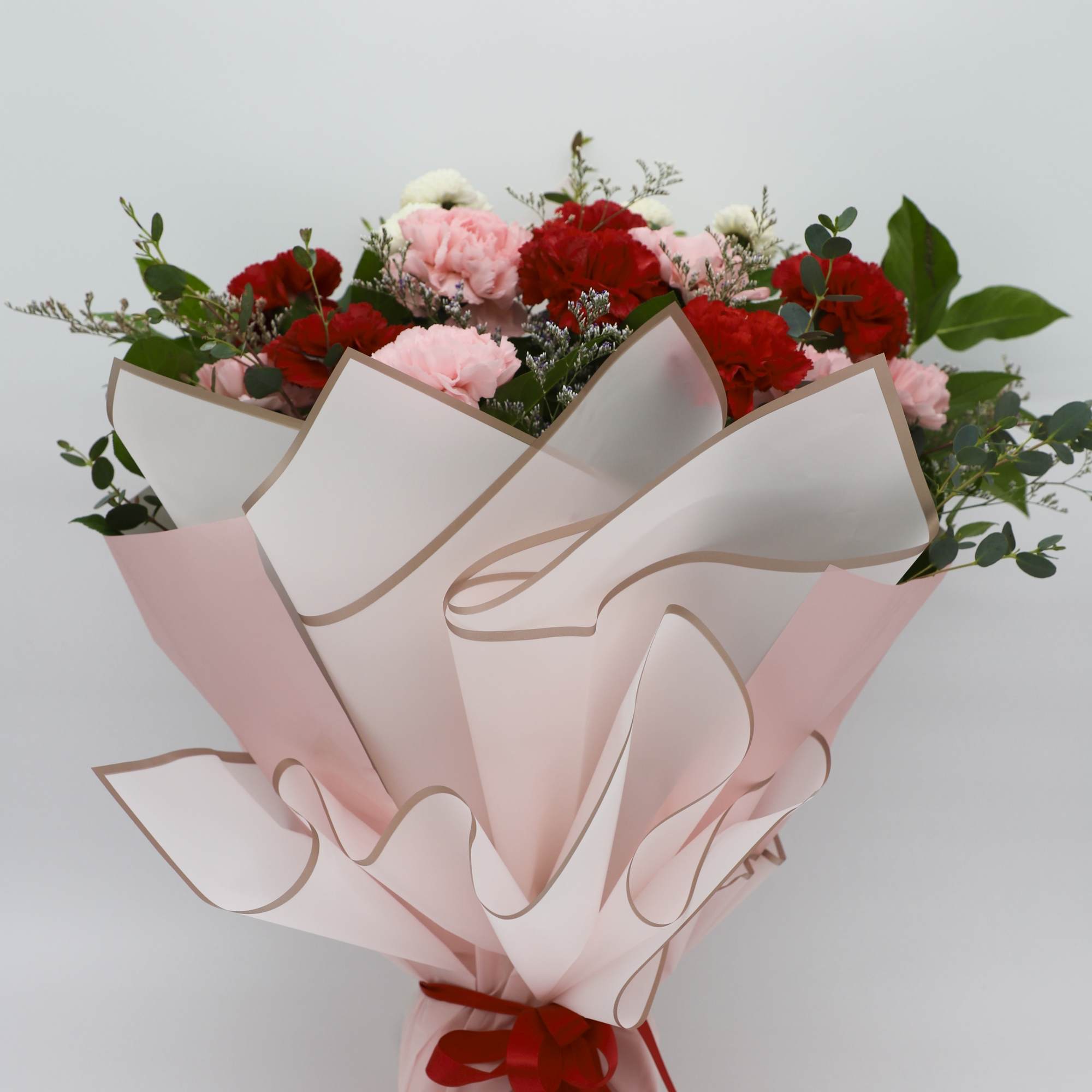 Bouquet of red and pink carnations wrapped in pale pink paper