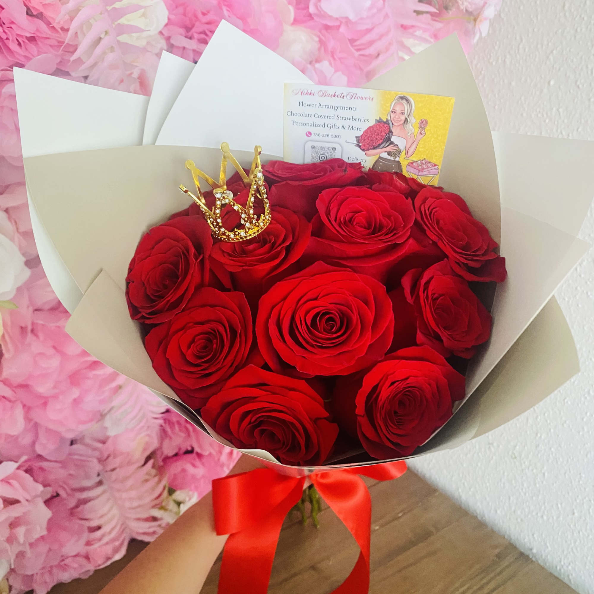 Bouquet of red roses wrapped in white paper with a red bow and a small gold crown accent.