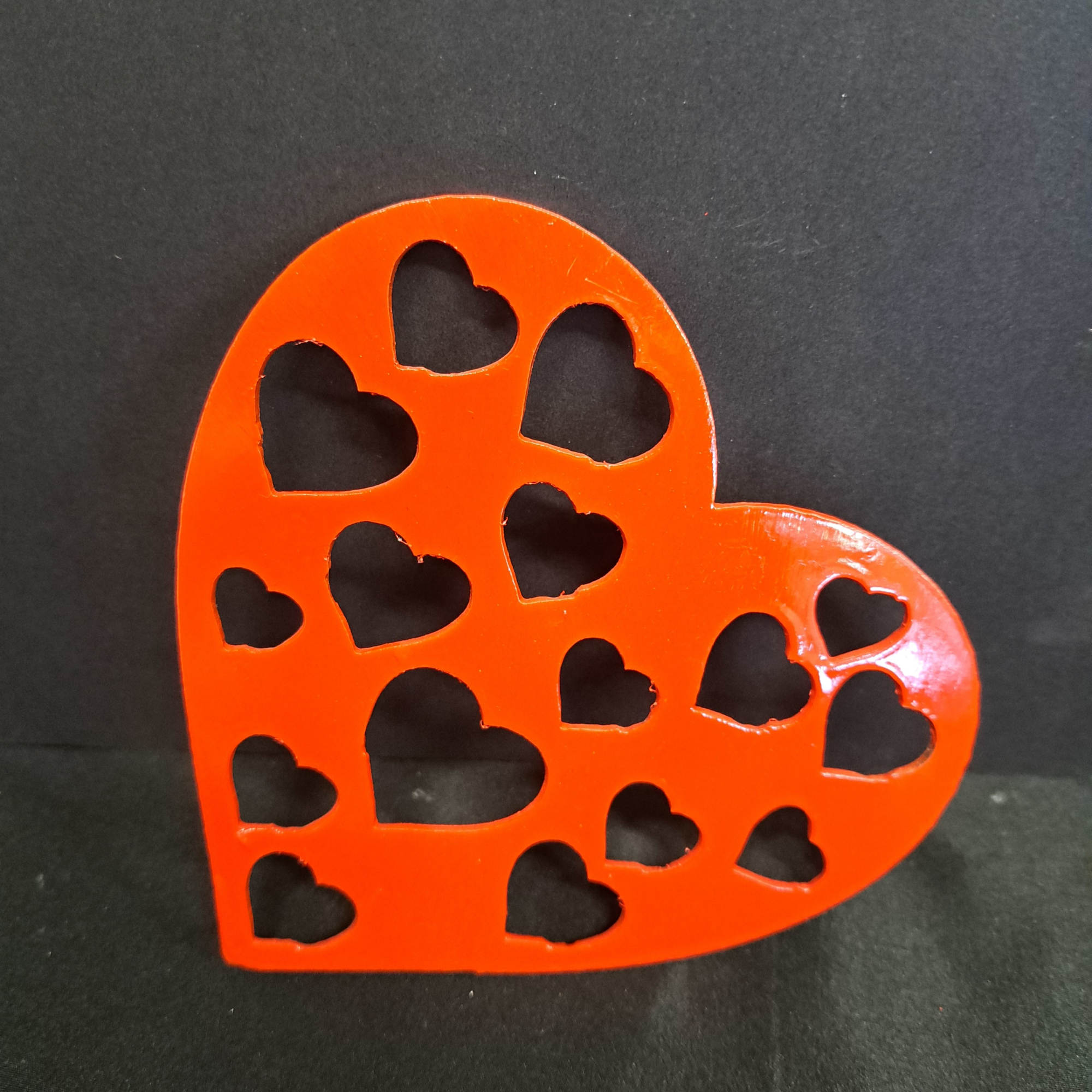 A glossy red heart-shaped metal wall hanger with playful heart cutouts brings