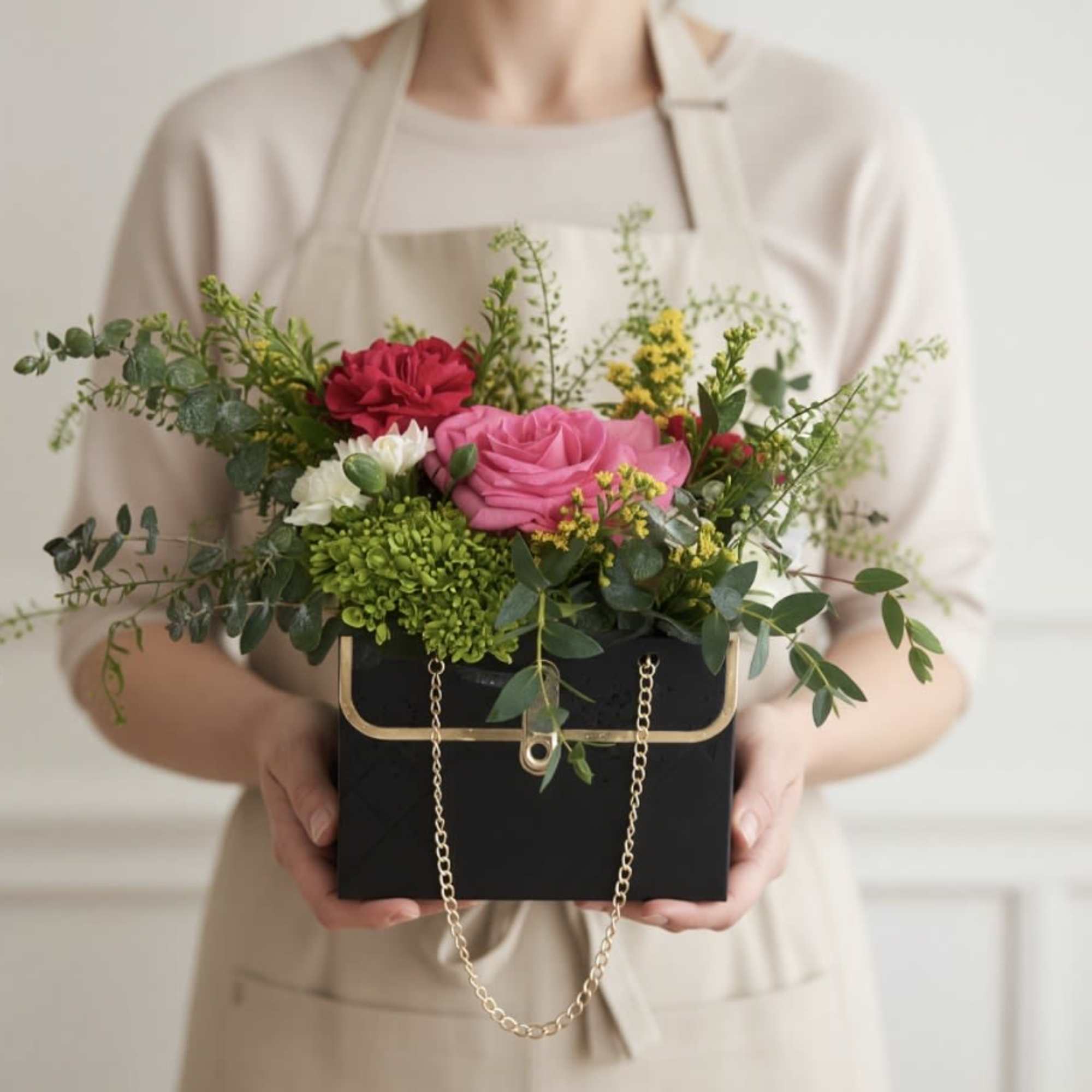 Mixed pink and red flowers in a black box with a gold chain handle