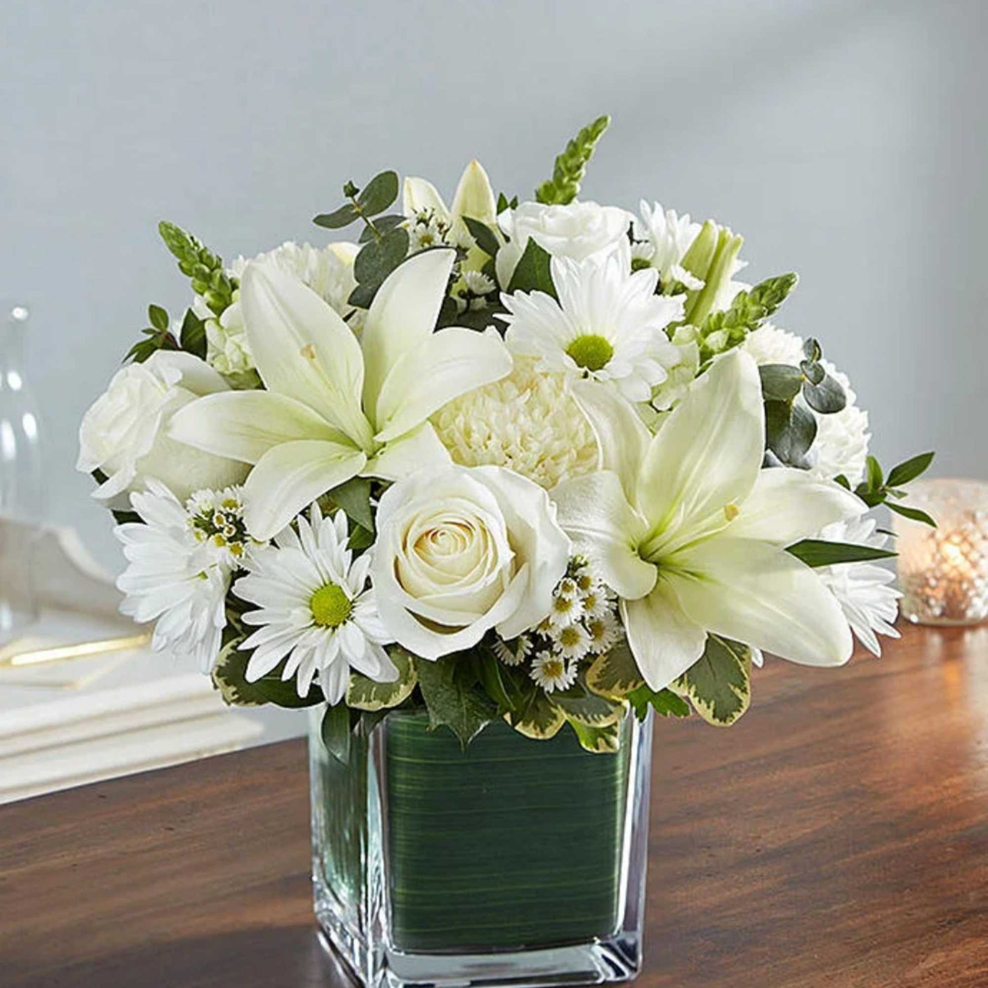 White lilies and daisies arranged in a square glass vase