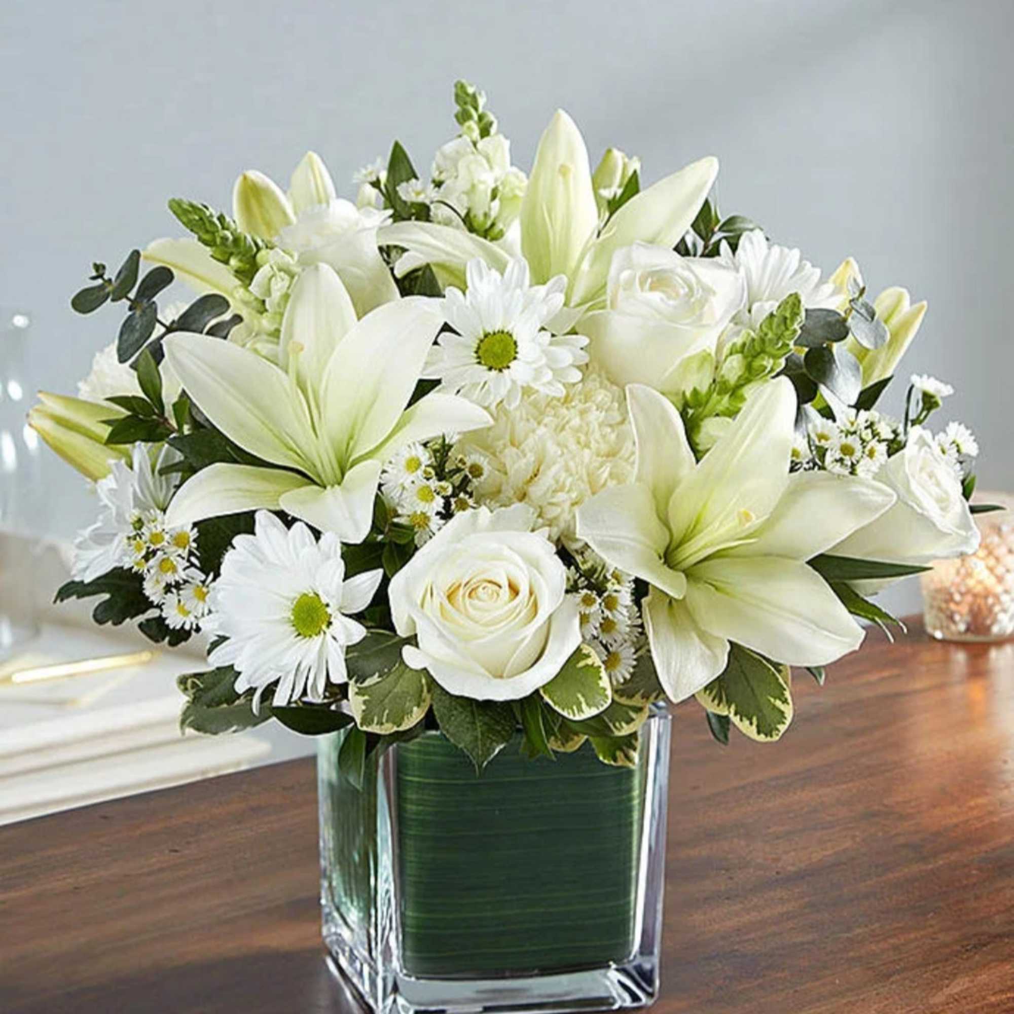 White lilies and roses arranged in a square glass vase