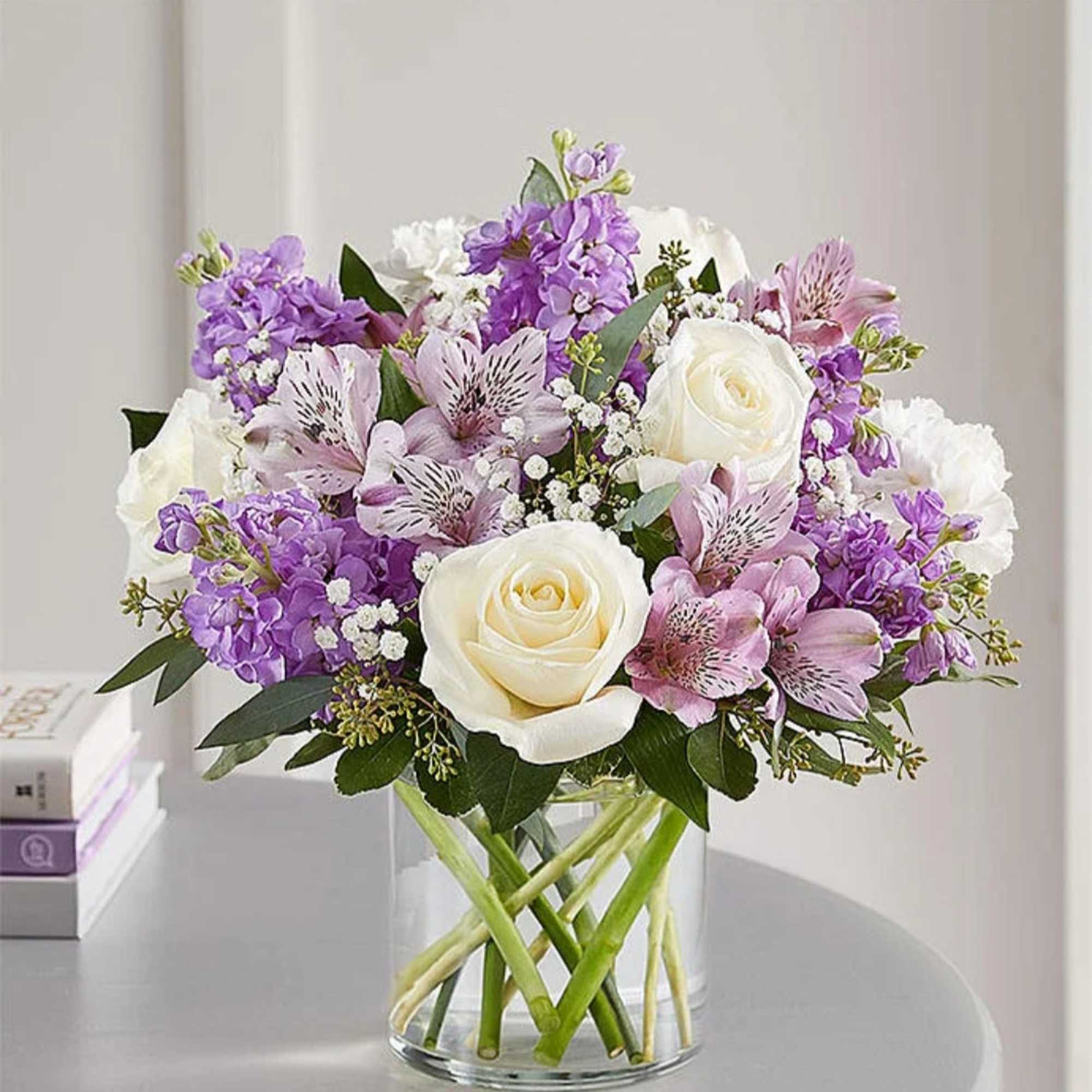 Bouquet of white roses and purple flowers in a clear glass vase