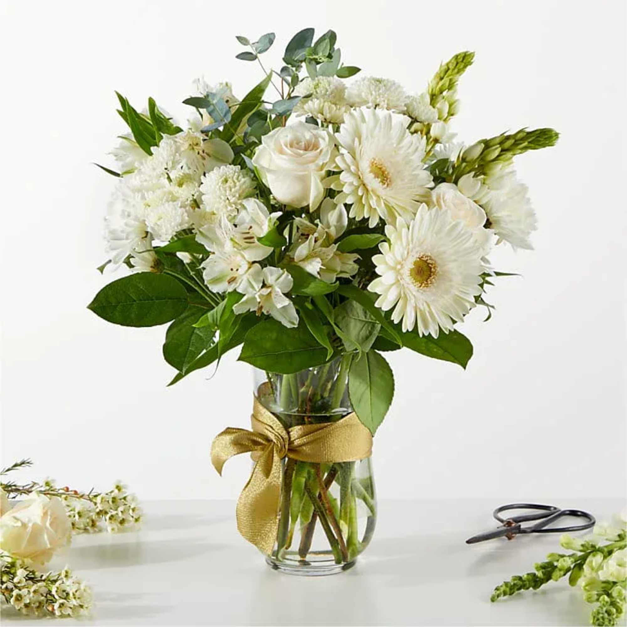 White flowers arranged in a clear glass vase with a gold ribbon